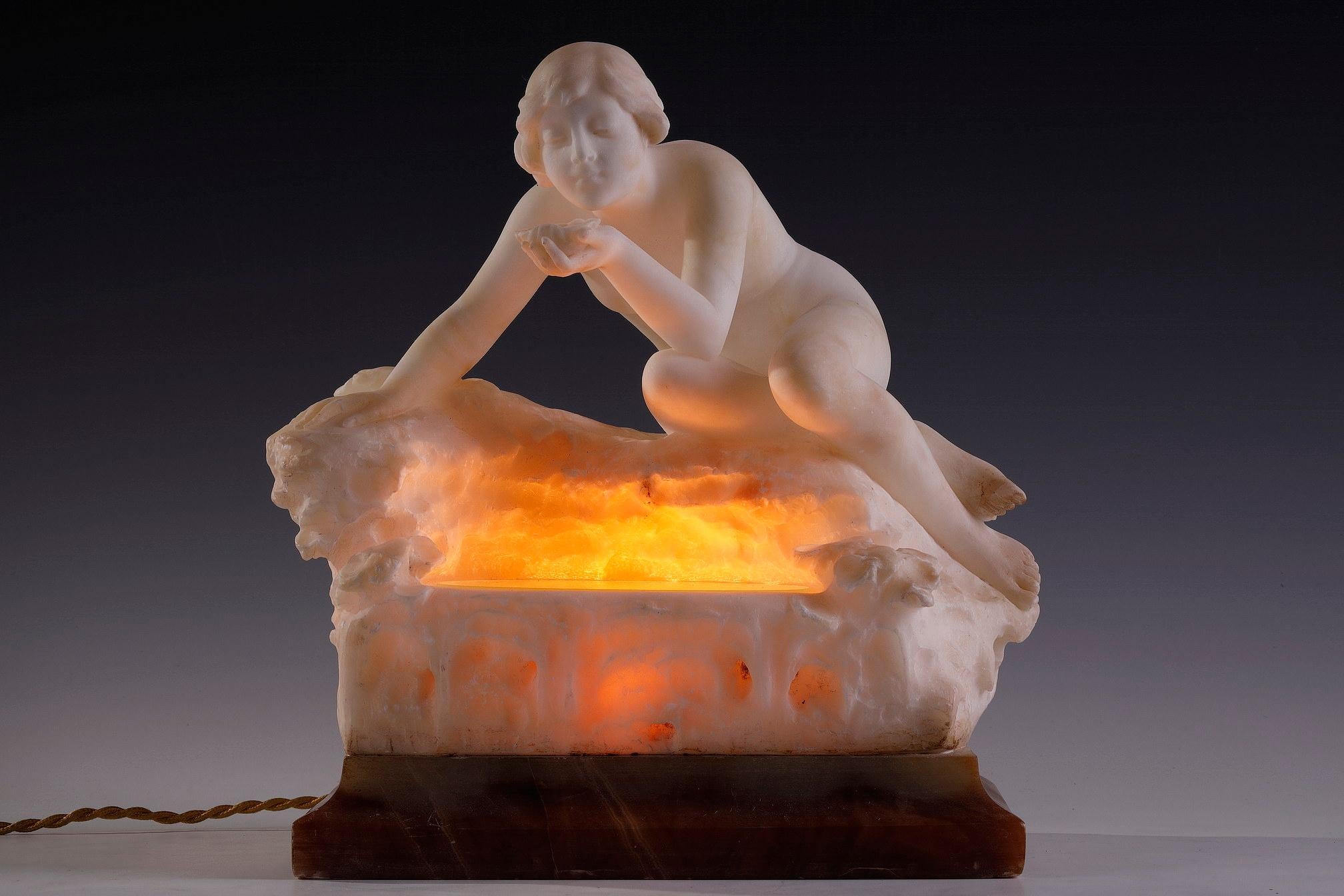 Signé sur la base Prof. G. Ca... ?

Charmante sculpture éclairante en albâtre représentant une jeune femme nue appuyée sur des rochers, et assise au bord d'une source dissimulant une lumière, recueillant l'eau avec un coquillage. Elle repose sur