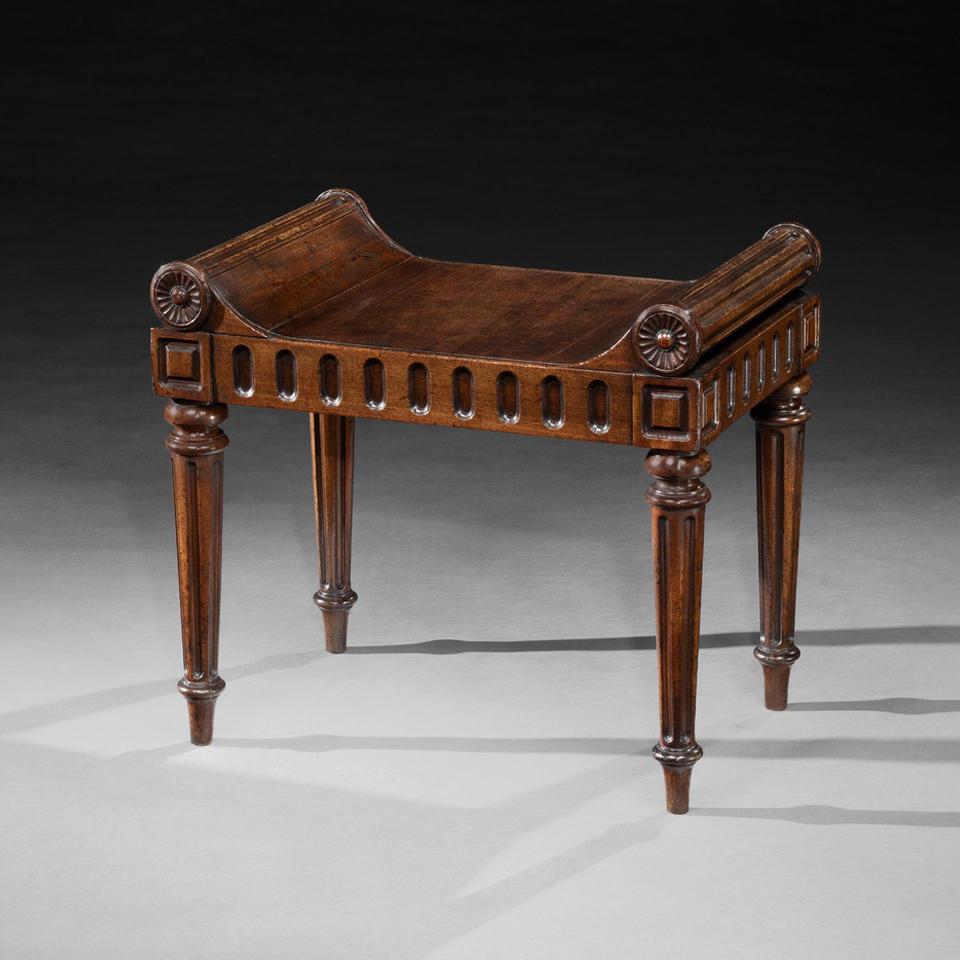 Ce beau tabouret de salle avec siège bombé en acajou massif présente de chaque côté un terminal à volutes cannelées terminé par une patère florale stylistiquement sculptée, au-dessus de rails sculptés avec des sculptures carrées à chaque coin,