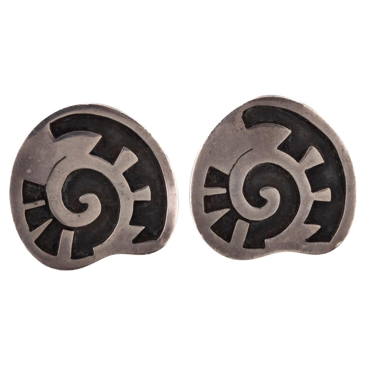 Silver Clip On earrings were designed by Margot de Taxco and show her identifying swirls and early Mexican silver hallmark. The earrings are raised sterling over an incised anodized silver pattern. The clip is comfortable with no pinch. Margot