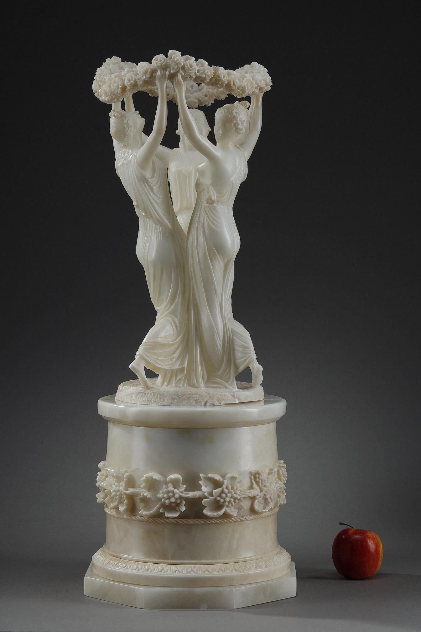 Alabasterskulptur, die die drei Grazien darstellt, die im Kreis tanzen und eine Blumenkrone halten. Die drei in griechische Tuniken gekleideten jungen Frauen werden auf individuelle Weise behandelt. Sie stehen auf einem hohen zylindrischen Sockel,