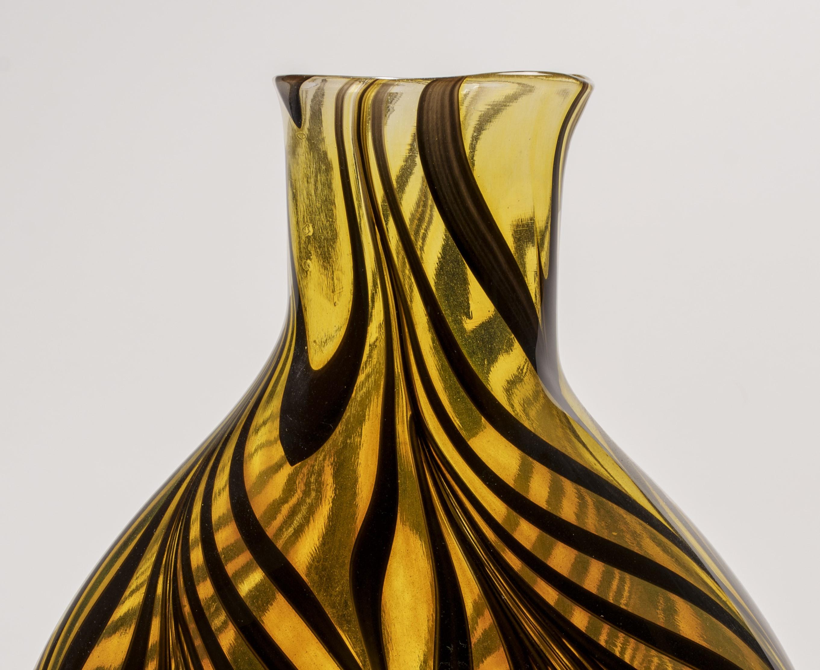Jeremiah Jacobs, a talented glassblower, has crafted a captivating blown glass piece using the festooning technique. This extraordinary artwork features a striking tiger pattern created with black festooning on a vibrant yellow amber glass