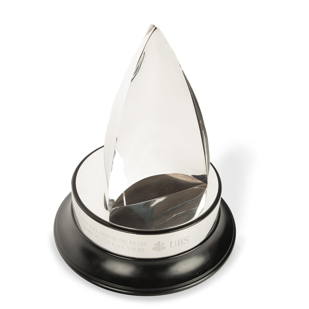The UBS America’s Cup Jubilee Race solid silver trophy by Theo Fennell, 2001. This striking trophy is of conical form, featuring three spinnakers on a downwind course, set on a circular ebonized plinth with a silver collar engraved with ‘UBS Jubilee
