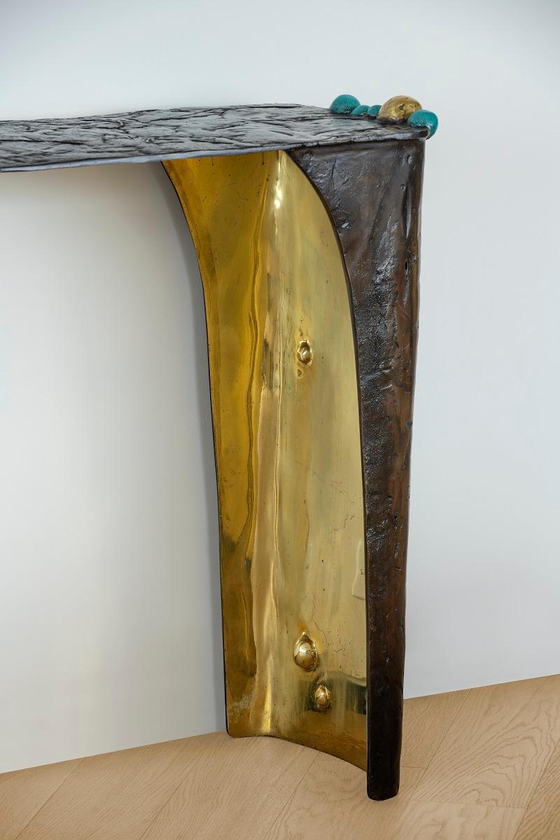La console d'ingresso, realizzata in bronzo stampato a caldo e patinato, emana un'eleganza di metà secolo con un tocco contemporaneo. Ogni pezzo è un capolavoro unico, creato attraverso l'applicazione di varie formule di patina sul bronzo, che danno