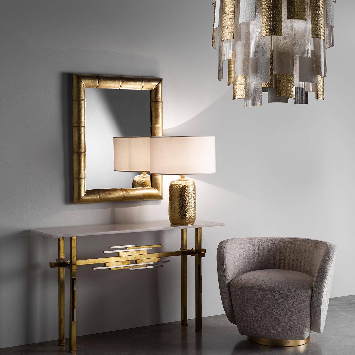 Metal with a brass finish and mouth-blown glass create a stunning chandelier of strong visual impact that exudes sophistication and modern allure. The structure features several layers of juxtaposed elements, slightly curved to follow the round