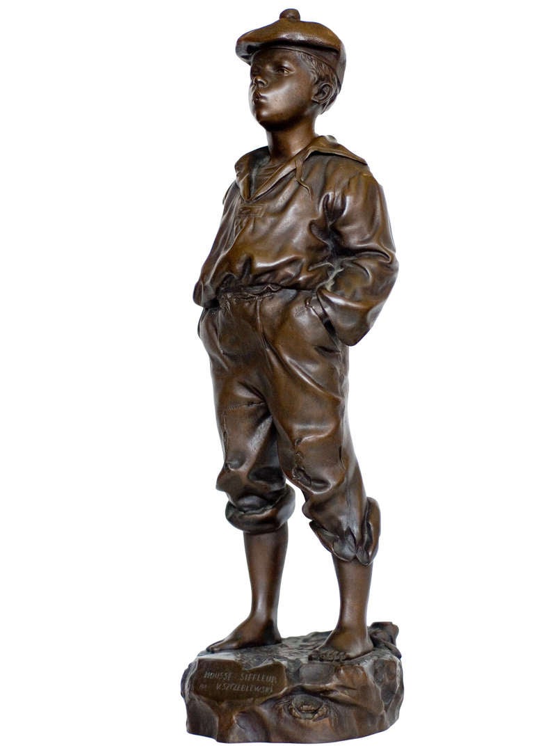 A cast bronze sculpture of a young barefoot boy. The boy stands nonchalantly with his hands in his pockets while whistling. He wears a cap and well worn clothes whose texture is highlighted by the bronze. 

This sculpture was originally created by