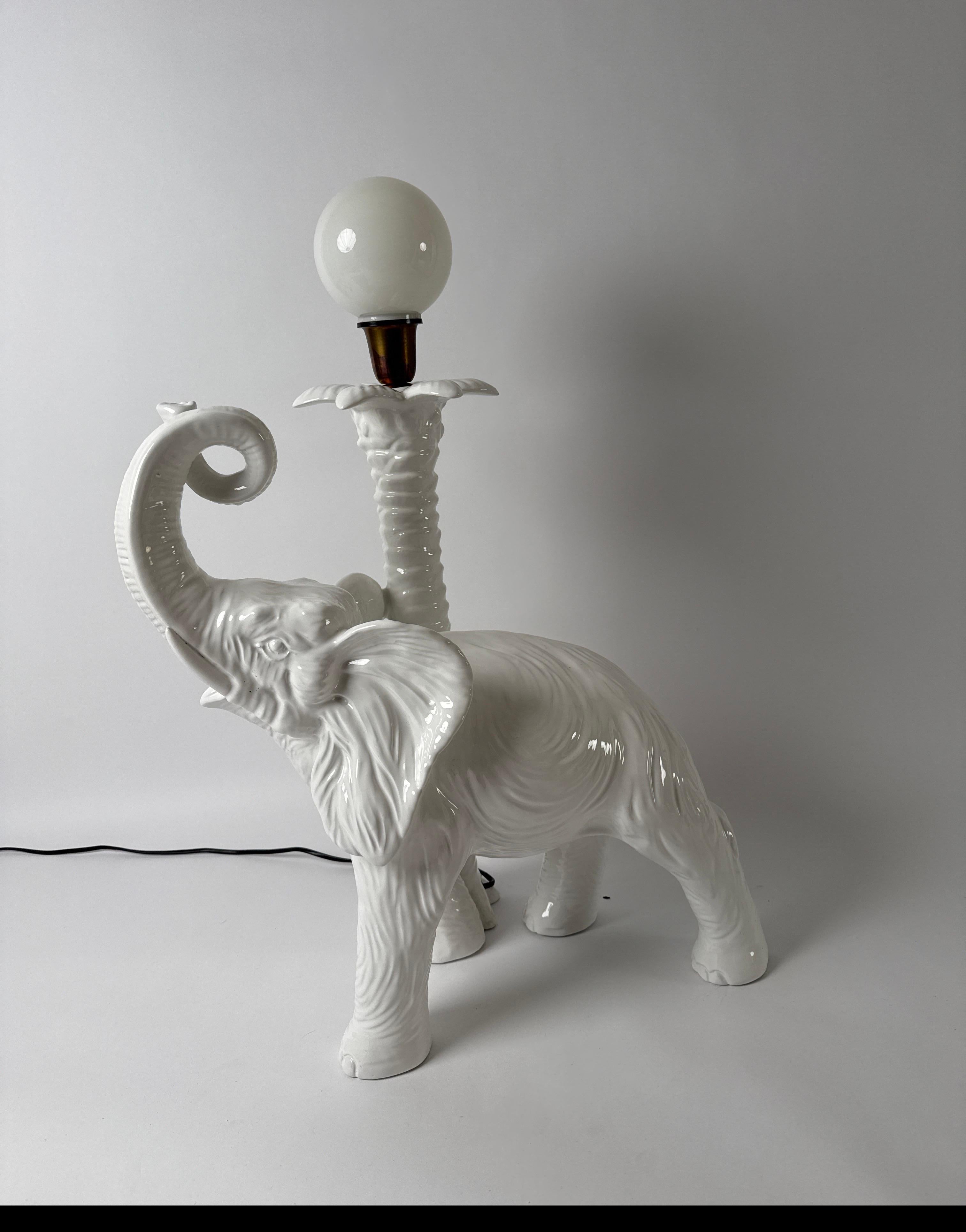 Lampe de table ou lampadaire élégante et intemporelle. Ce magnifique lampadaire élégant est une rareté et extrêmement élégant et beau. Le bel éléphant s'appuie sur un palmier et lève sa trompe vers le ciel. Une boule de verre repose sur le palmier