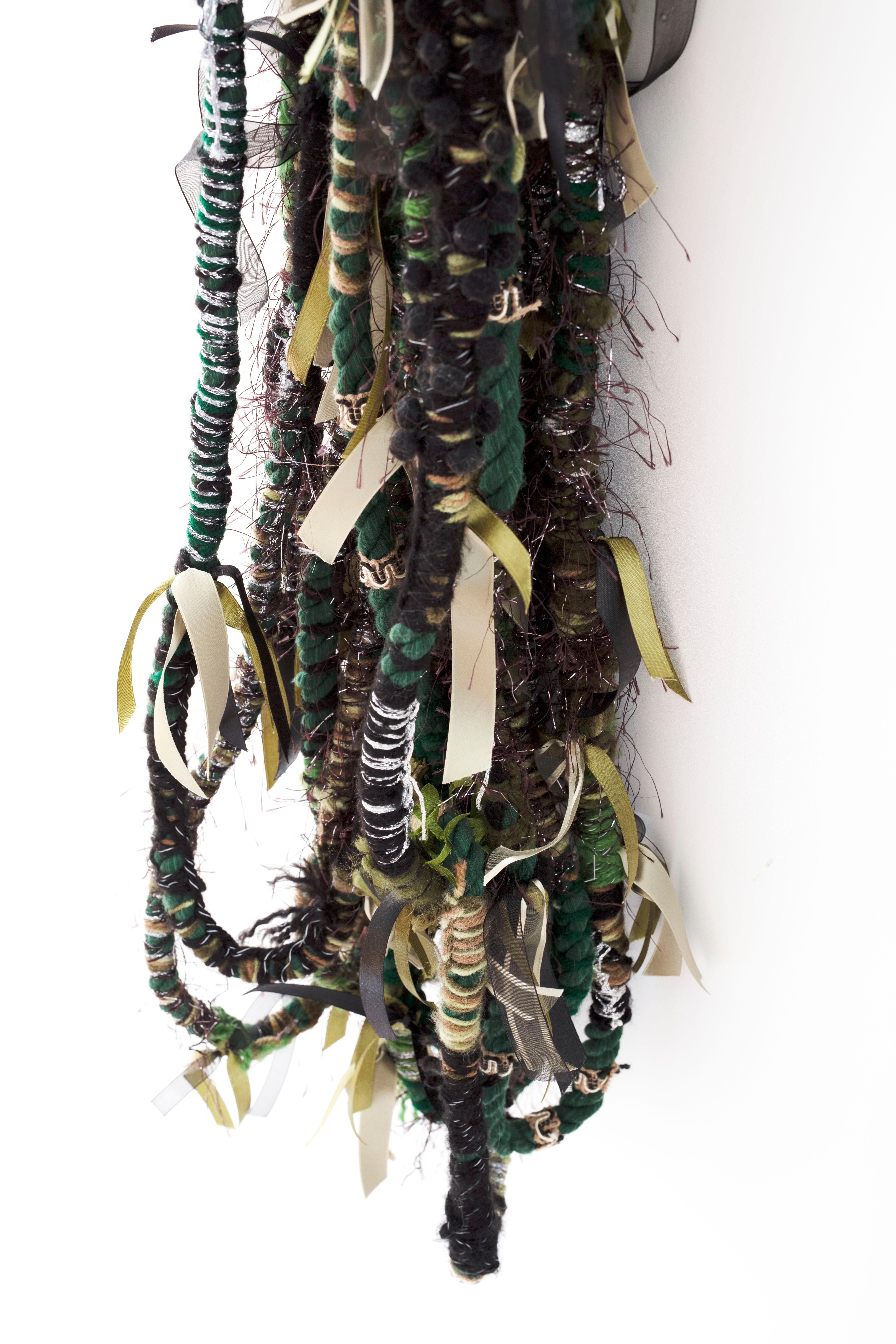 Extensions of rope, impeccably wrapped, woven, tied and embellished with recycled beads, zip ties, ribbon, lace, tape and beads lure you into a hue-imbued, installation symbolizing natural hair. These whimsical fiber sculpture gingerly invites the