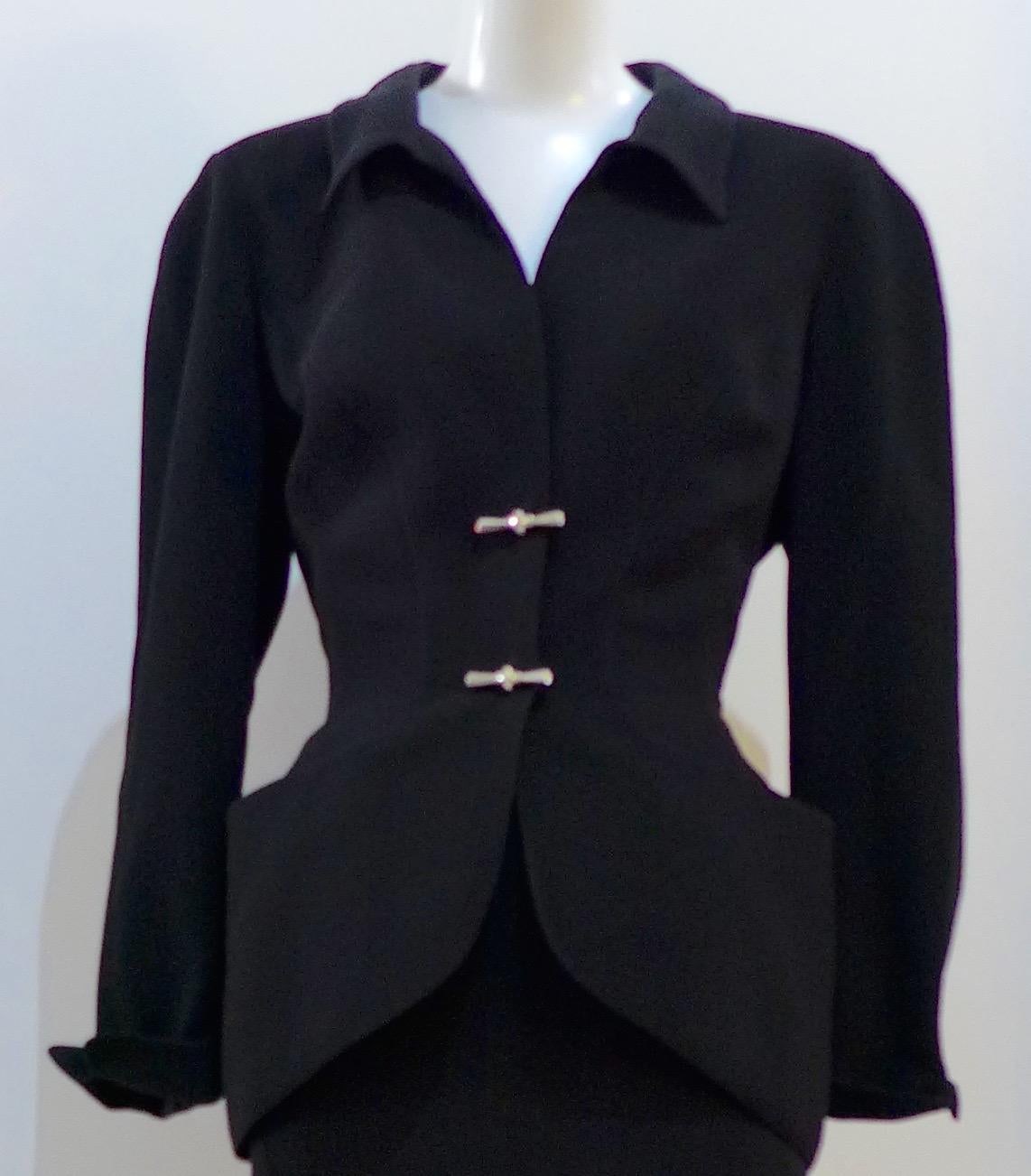 This THIERRY MUGLER skirt suit is composed of a black polyester fabric. Features a classic Mugler silhouette with nipped waist and curved bust-line to neckline design. The jacket has front snap closures, rounded shoulders, and silver and rhinestone