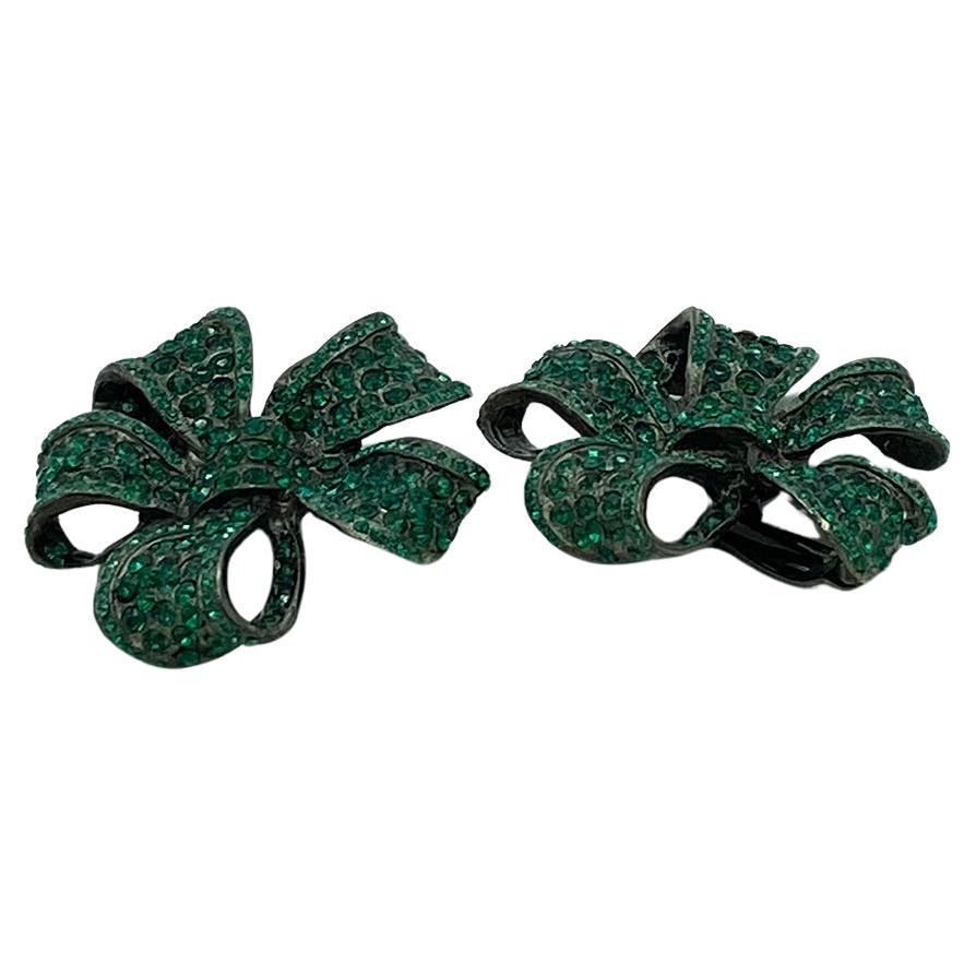 This is a pair of Thelma Deutsch green ribbon earrings. These statement clip on earrings has two different sized pave green rhinestones set on a gunmetal background that creates the depth of the ribbon. They are filled with holiday spirit!

Thelma