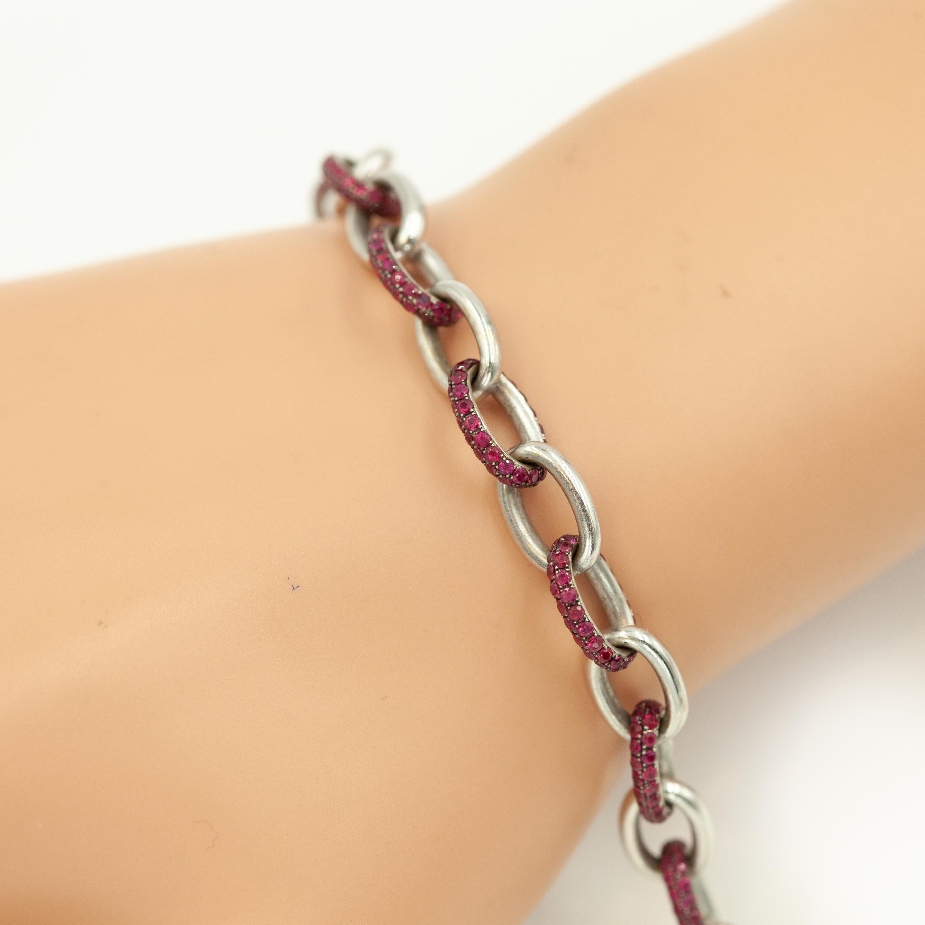 Este lujoso brazalete, un diseño atrevido y distintivo del famoso joyero británico Theo Fennell, está fabricado en oro blanco de 18 quilates y engastado con rubíes rojos intensos. Cada eslabón ovalado alterna eslabones de oro blanco pulido y