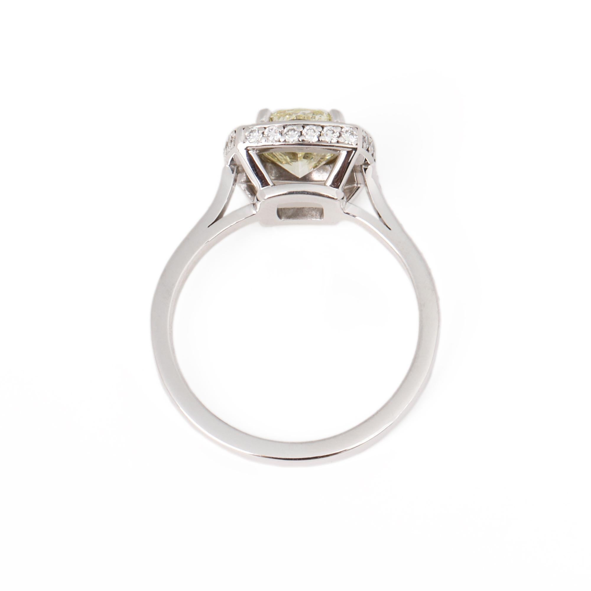 This ring by Theo Fennell is a bespoke design and features a central 1.57ct natural yellow cushion cut diamond surrounded by a halo of round brilliant cut diamonds with further diamonds along the shoulders set in 18ct white gold. UK ring size K 1/2.