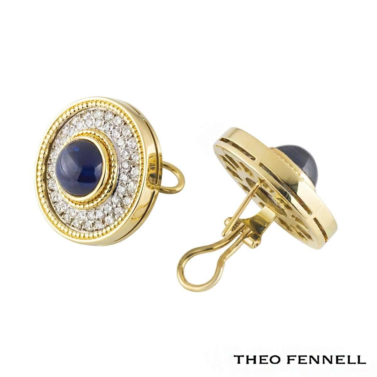A pair of 18k yellow gold earrings by Theo Fennell. Each circular earring features a 1cm cabochon cut deep blue sapphire in a rubover setting complimented by a beaded outer edge. Surrounding the central stone are 48 round brilliant cut diamonds,