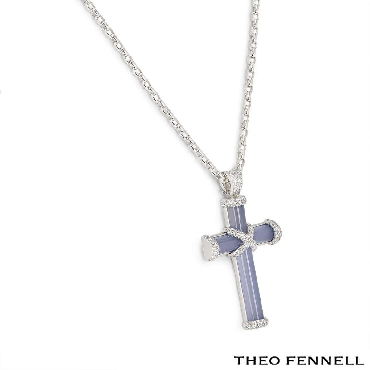 An 18k white gold cross pendant by Theo Fennell. The pendant is formed of a polished blue semi-precious gemstone cross with pave set diamond accents totalling approximately 0.90ct. The cross measures 3.5cm in width, 6.5cm in length and comes on a