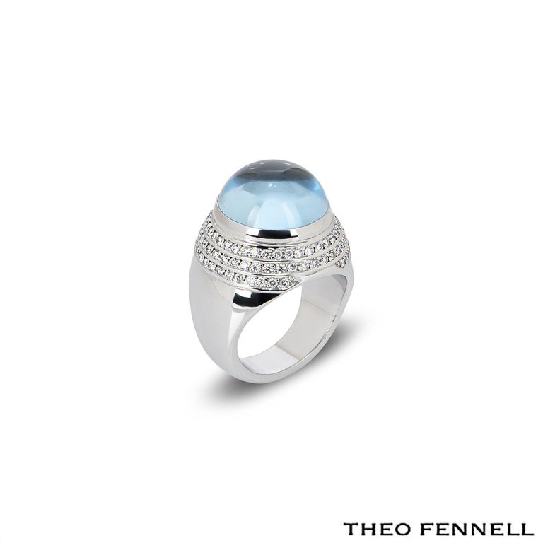 A fashionable Theo Fennell diamond and aquamarine ring from the Whisper collection. The ring comprises of a cabochon cut aquamarine in a rub over setting, complemented by 3 rows of round brilliant cut diamonds. The diamonds have an approximate