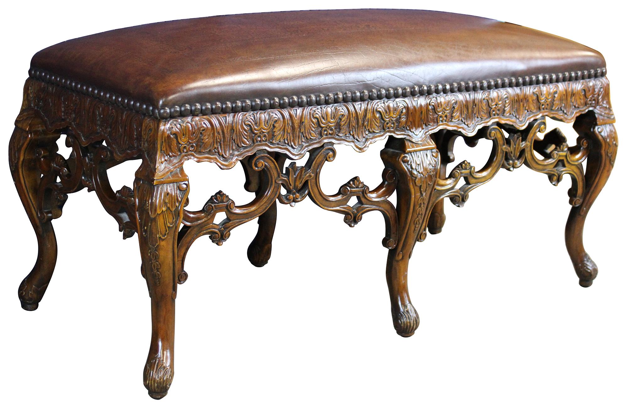 Vintage tooled leather and carved mahogany bench by Theordore Alexander. Features ornate scrolled carvings with floral, shell and acanthus motifs and nailhead trim around the leather. The cabriole legs terminate into scrolling acanthus designed