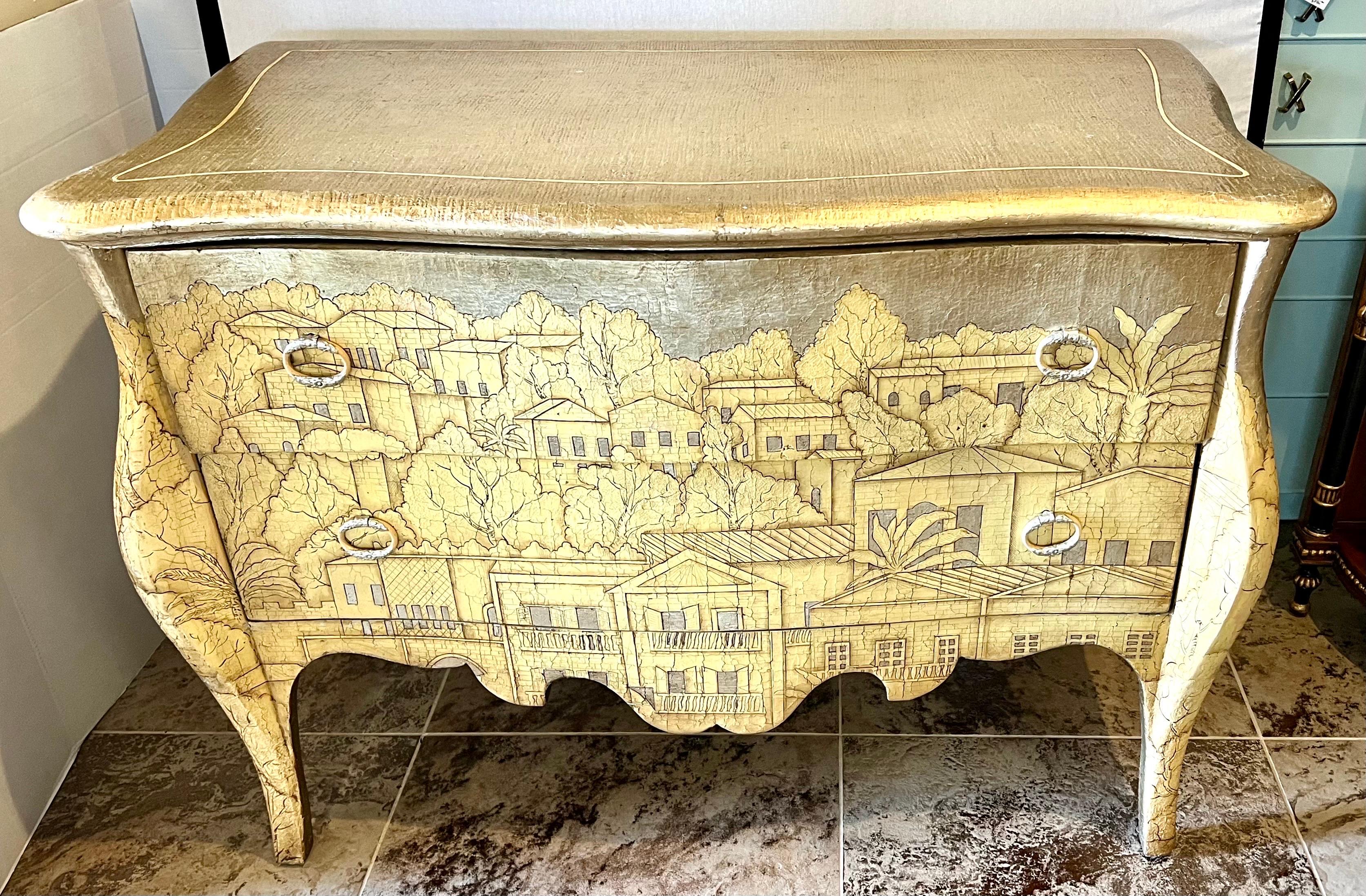 Stunning one-of-a-kind Theodore Alexander bombay chest with two spacious drawers features hand carved landscape of houses on the front and sides. Besides the carvings, what makes this piece so unique is the color and silver leaf finish. Even the