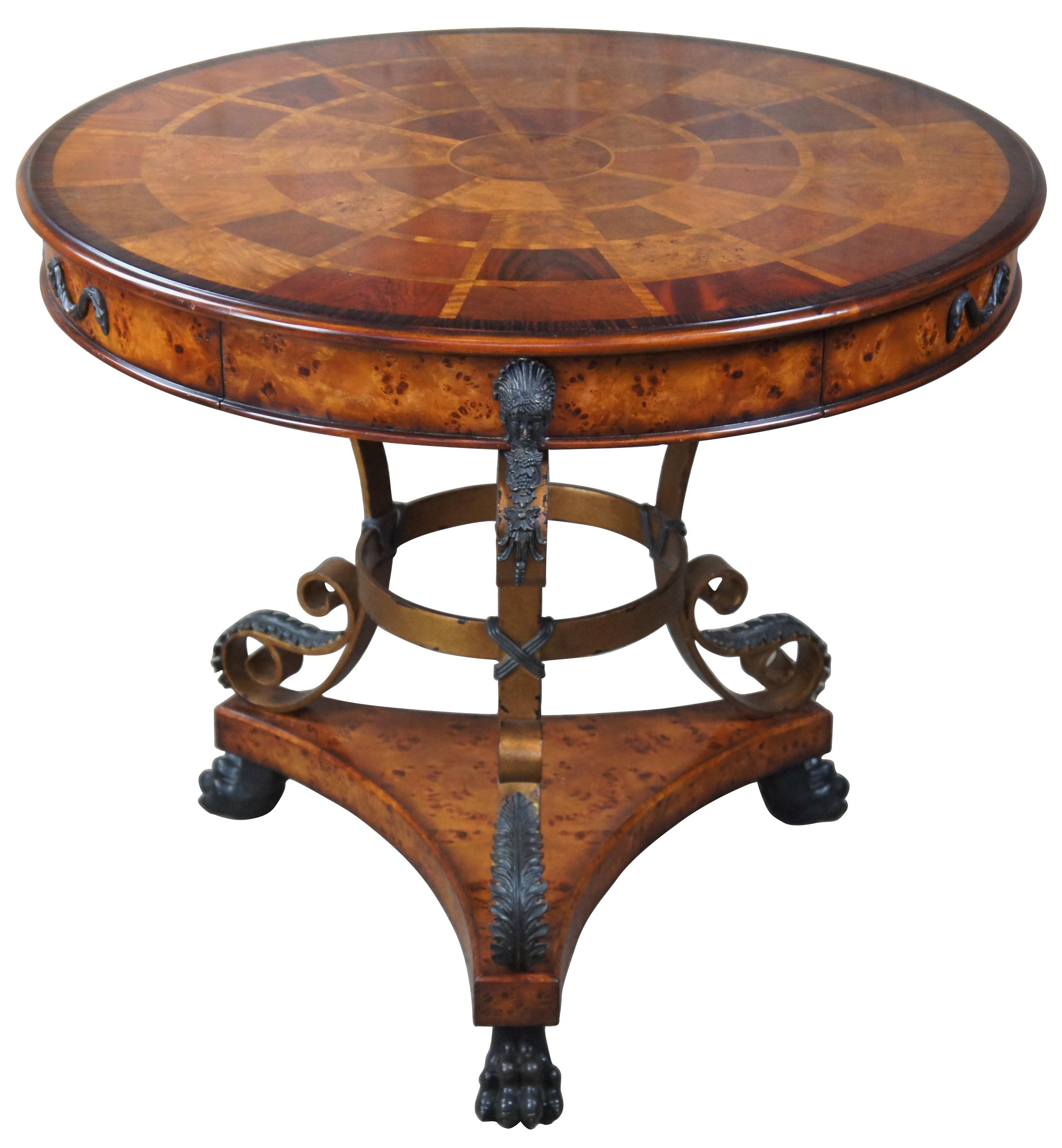 Theodore Alexander entryway center table with a gilt iron base leading down to paw feet. The vibrant top is amplified by the use of mahogany and walnut in a circular banded pattern framed in Dark Morado. The drum shaped apron includes three drawers