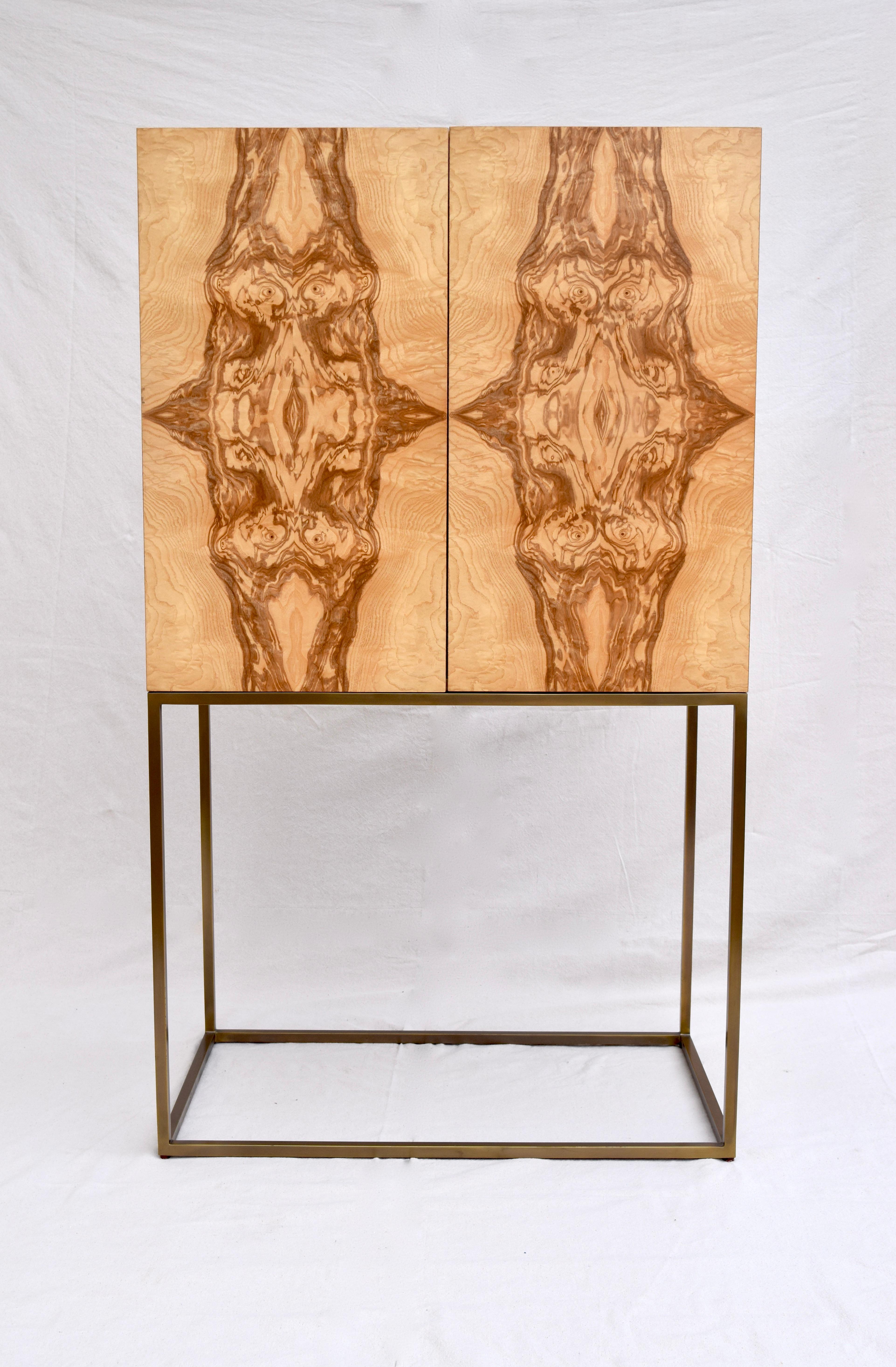 A striking Theodore Alexander Keno Bros. Collection burl ash and brass base bar cabinet. So many features include interior light, brass stemware storage, single adjustable clear glass shelf and Hollywood Regency distressed styling to the Harlequin