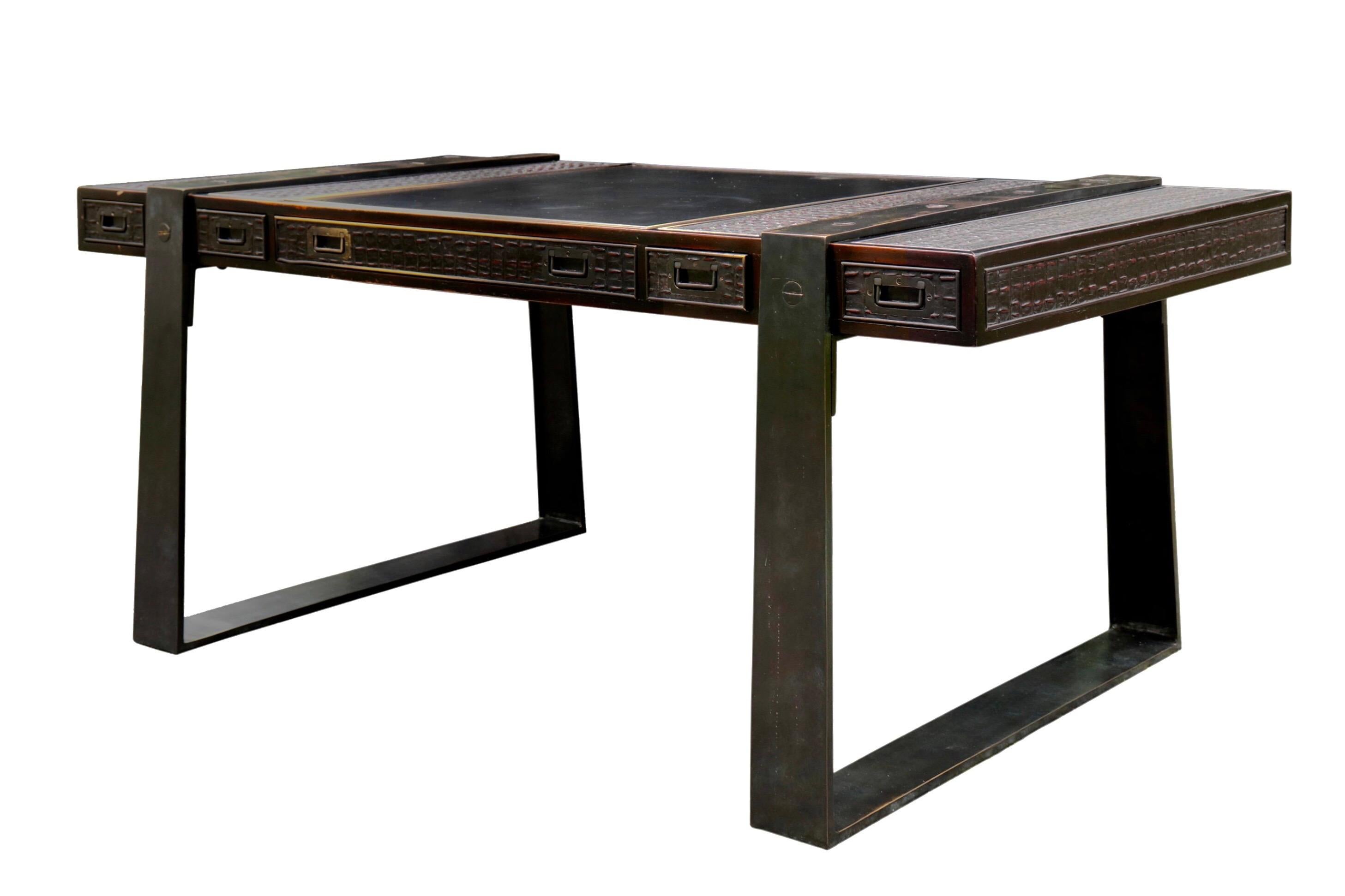 A campaign style partners desk made by Theodore Alexander. The table top has a large central black leather writing area and is supported with two trapezoid shaped brass legs in a black finish. Five drawers on each side open with recessed campaign