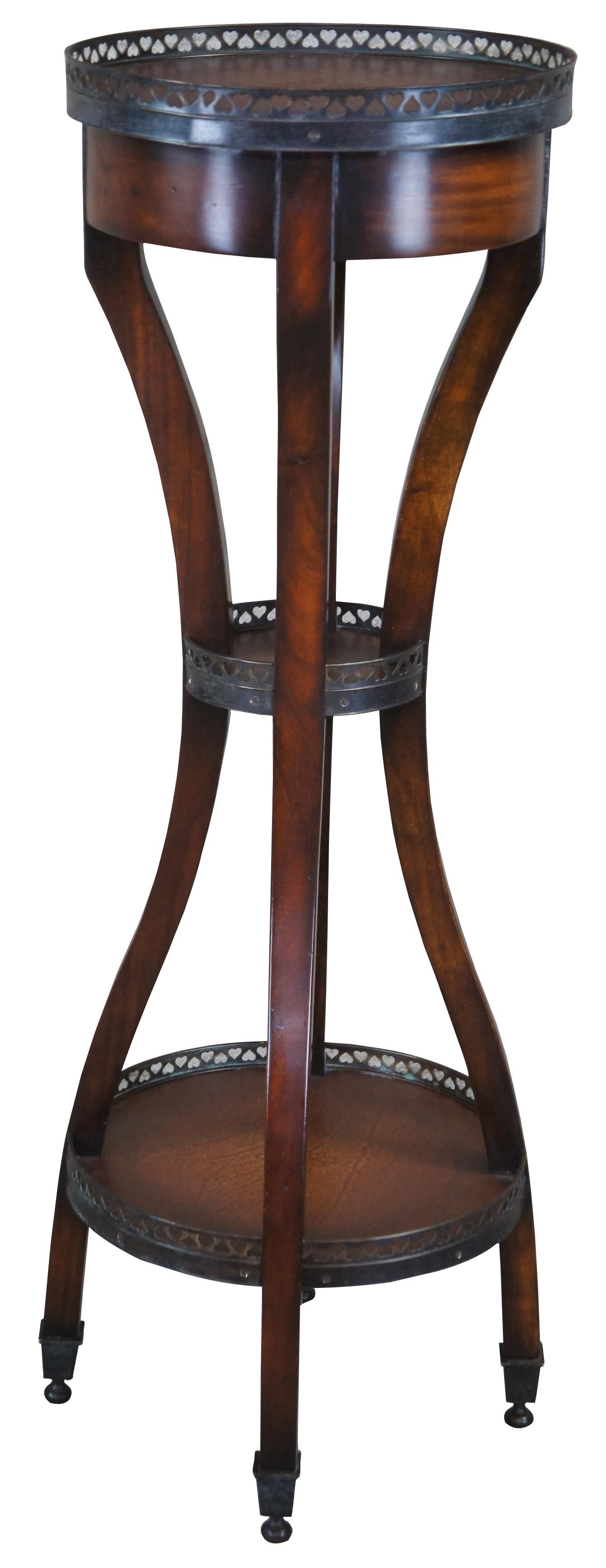 An elegant display table by Theodore Alexander. Made from mahogany with elongated legs offset by a round 3 tier design of pierced heart shaped galleries and tooled leather tops. Rests upon square capped bun feet.
 