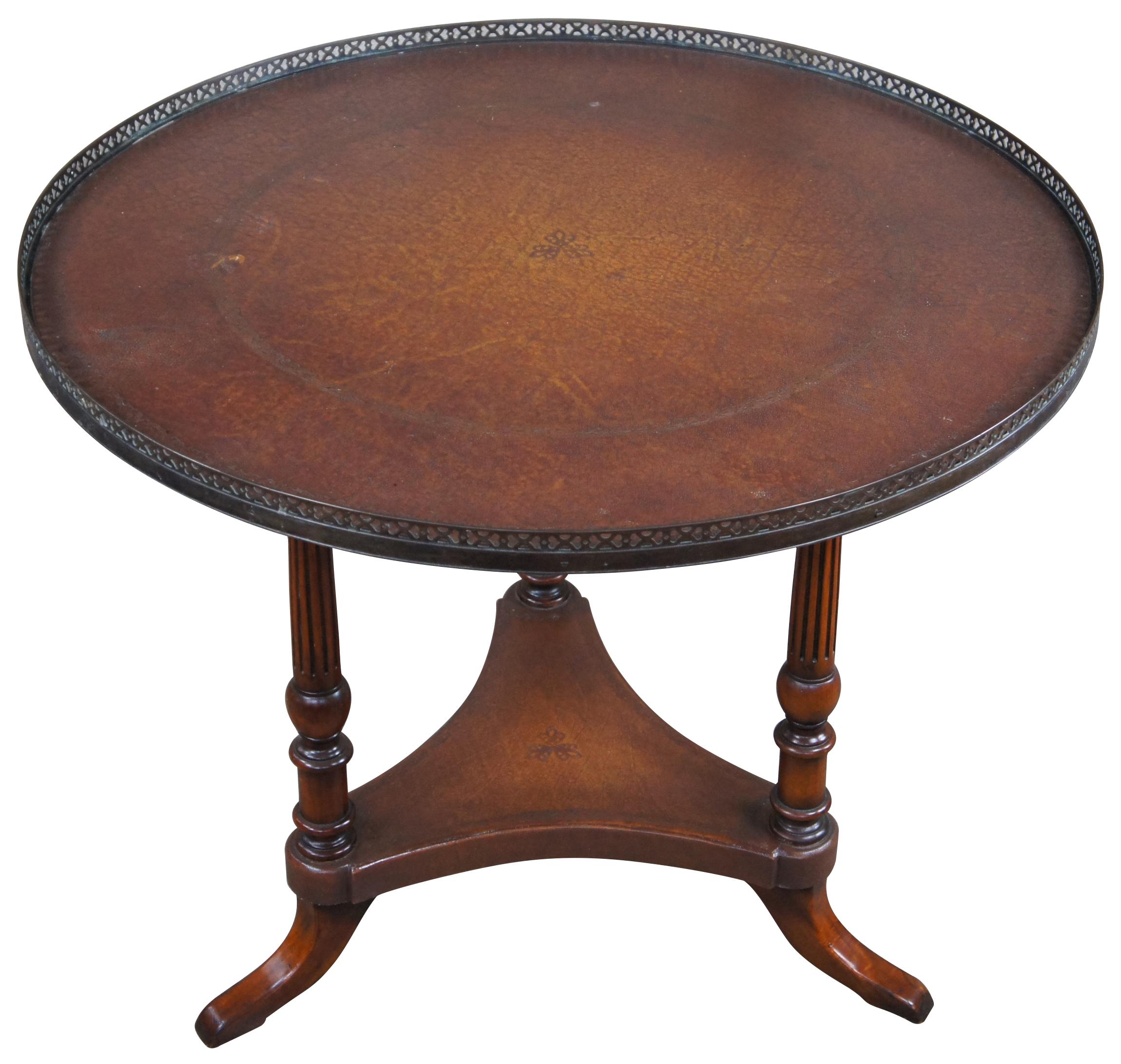 Theodore Alexander tooled leather and mahogany center table. Drawing inspiration from Traditional and Sheraton styling. Features a round top with pierced brass gallery supported by turned and fluted columns with a tripod base. 
 
