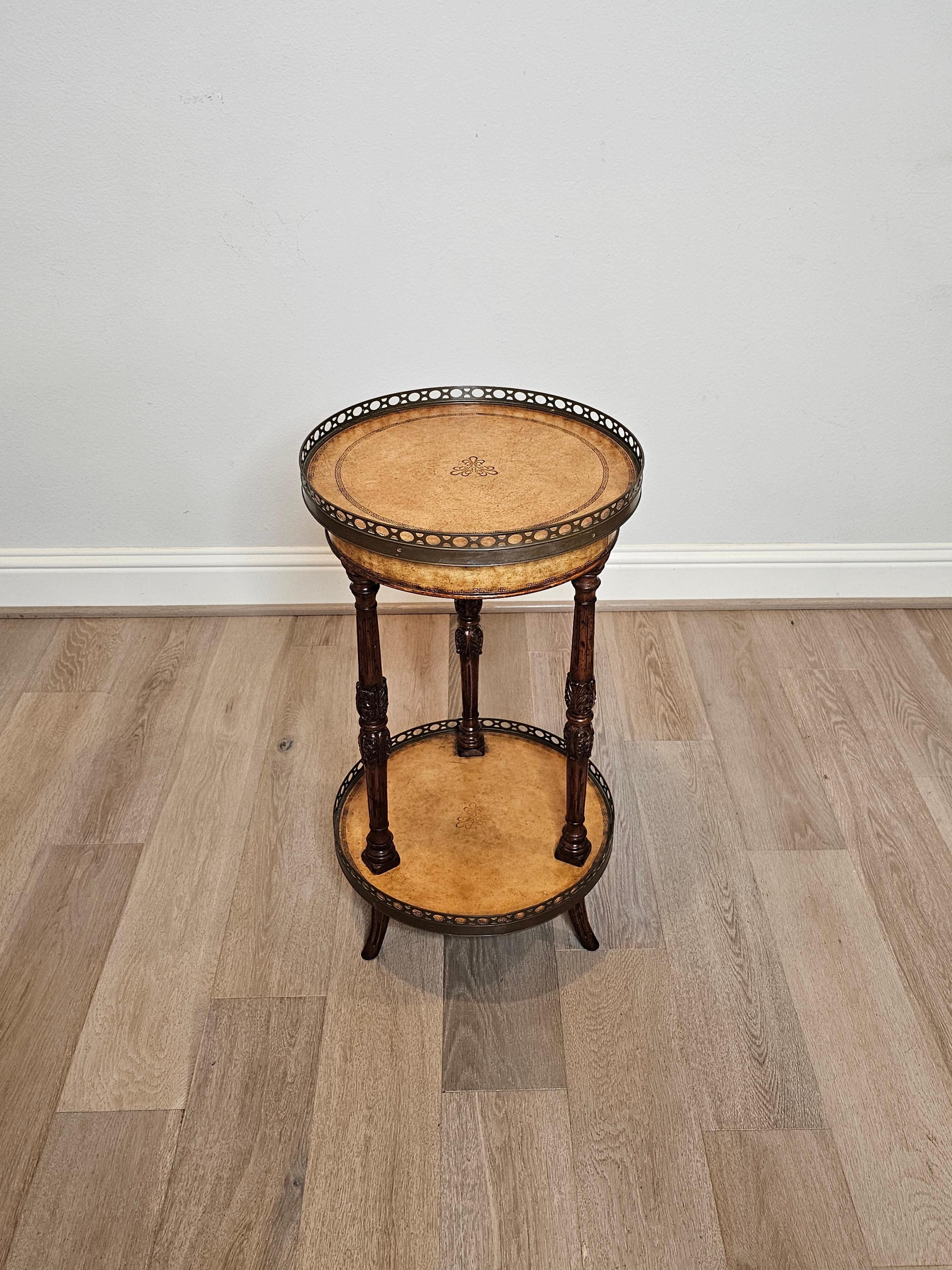 A lovely Regency style two-tier side table, attributed to fine quality luxury designer Theodore Alexander, late 20th century.

Having round tan leather tops with embossed Greek key border and Bouillotte style raised pierced metal galleries, inset