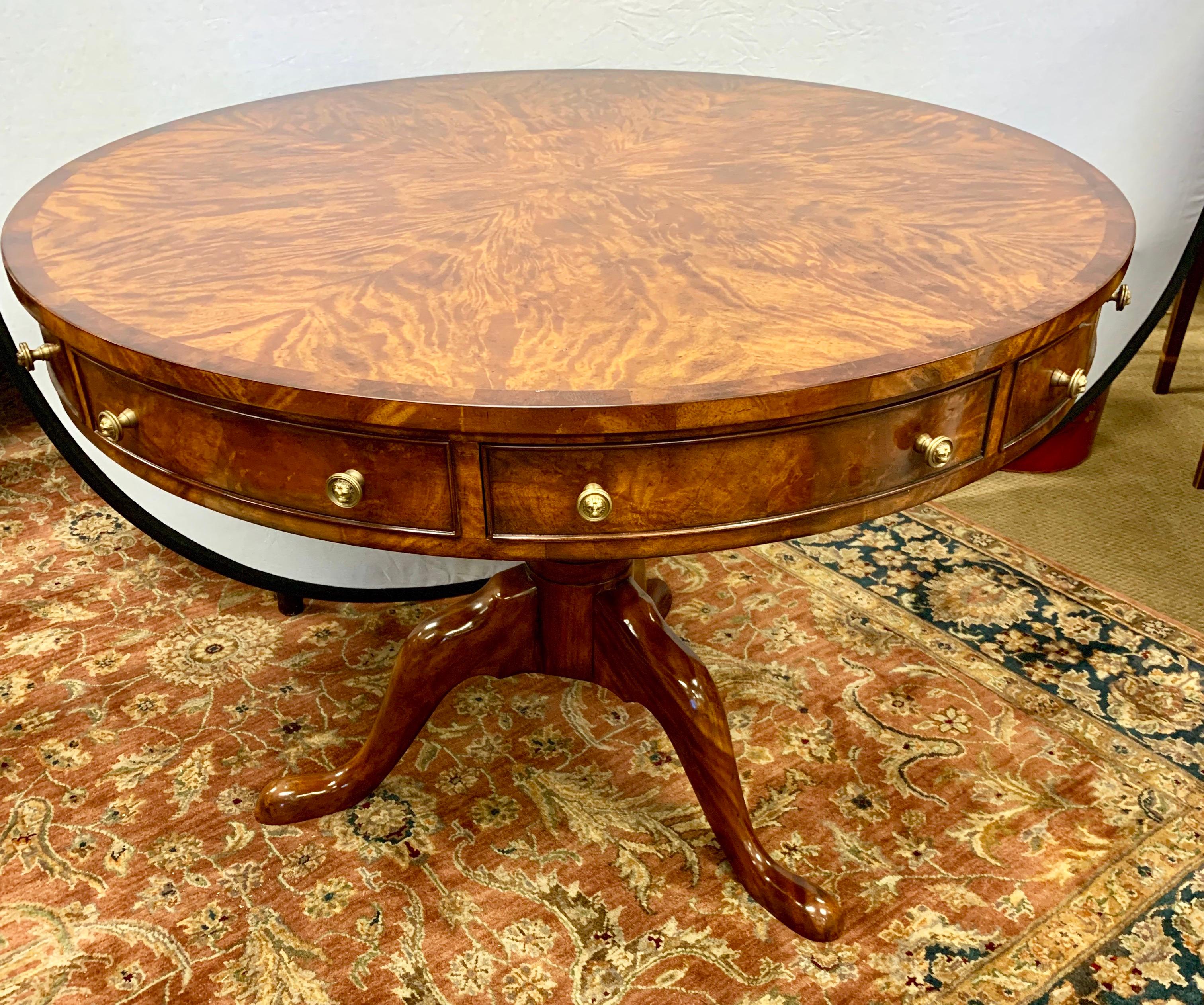 Stunning Theodore Alexander Althorp flame mahogany round center table with four working drawers and four faux drawers with round brass lion pulls. It sits on a tripod pedestal base. Perfect as a center table but can also be used as a game or