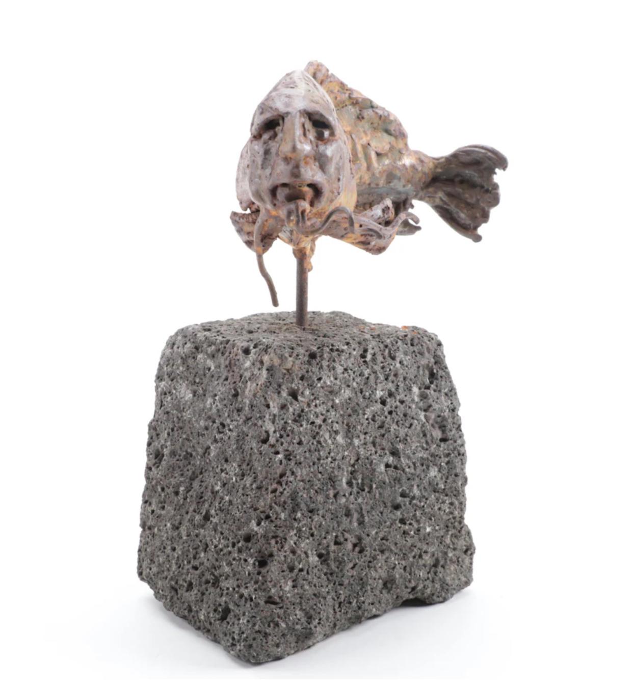 Thought provoking sculpture of a type of fish with the face of a man by Theodore Gall, 1987. Mounted on a chunk of lava rock, the fish has incredible patina that was applied by the artist, interesting catfish type feelers and the face of a seemingly