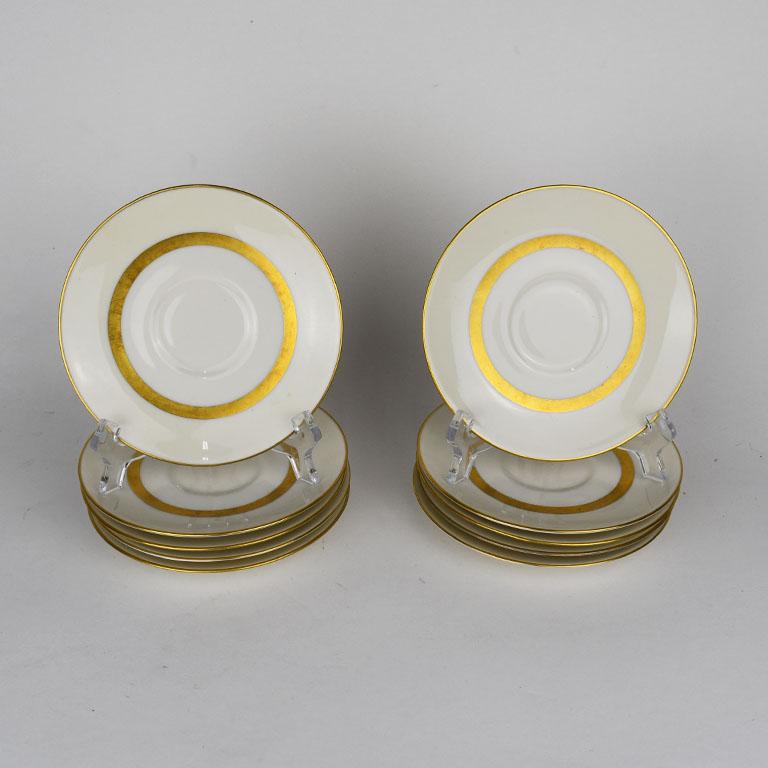 A set of 10 ceramic plates by Gotham by Theodore Haviland. Each saucer is in a light cream white hue, and features a thick gold painted band around the center as well as on the interior. Marked at bottom:
Theodore Haviland 
New York
Made in