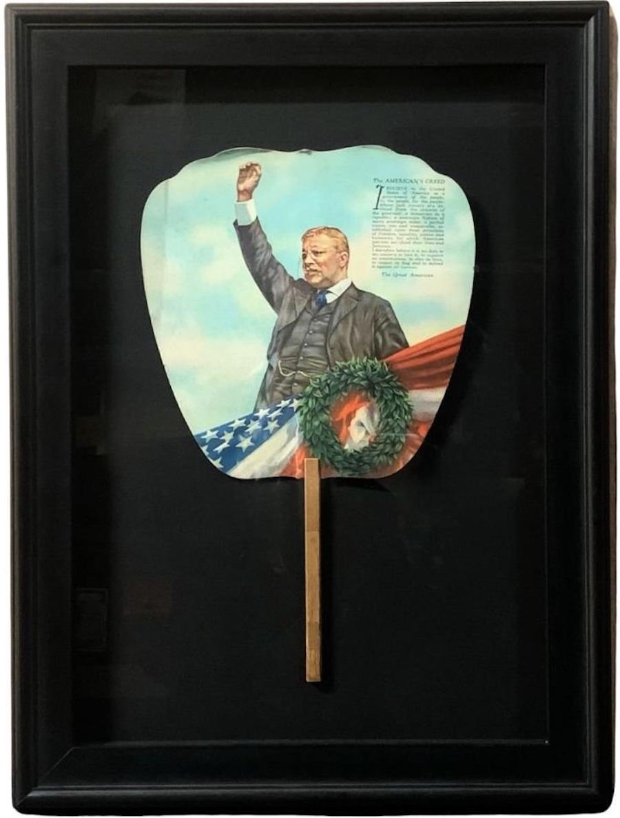 Presented is a patriotic printed paddle fan, with an image of Theodore Roosevelt giving a speech in front of a laurel wreath and patriotic bunting. Above him is the printed text of “The American’s Creed.” “The American’s Creed” was written by