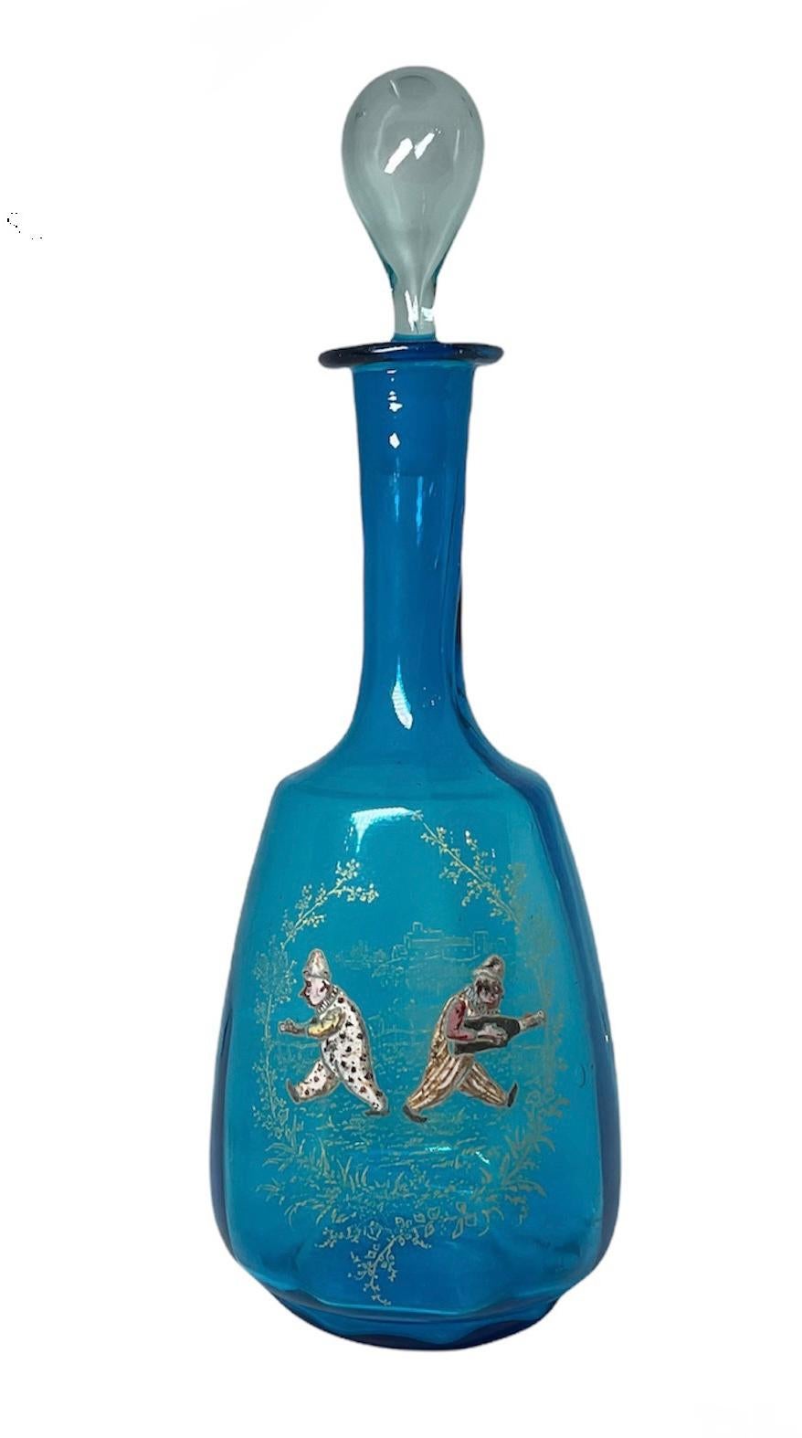 This is a Theodore Rossler bohemian hand blown royal blue glass wine decanter. It depicts two clowns walking in opposite direction in a country landscape with a wood fence and some foliage around them, using the “Color Cake” enamel technique. One of