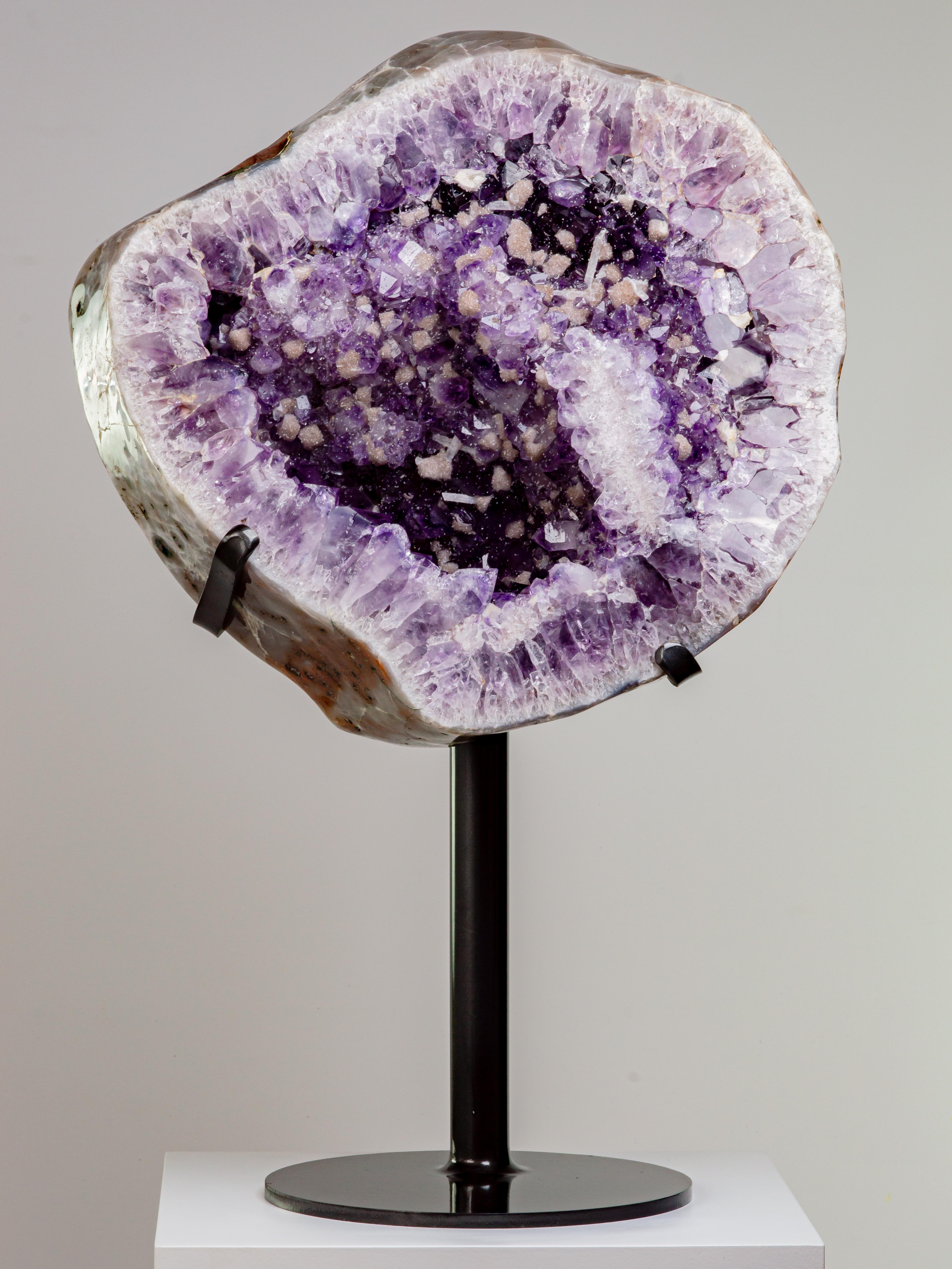This striking circular slice preserves the end of a large geode. Lined with deep
purple, high peaked amethyst crystals, this wonderful piece is punctuated with
small calcites overlaid with druzy quartz, resembling snowballs. Further sprinkles
of