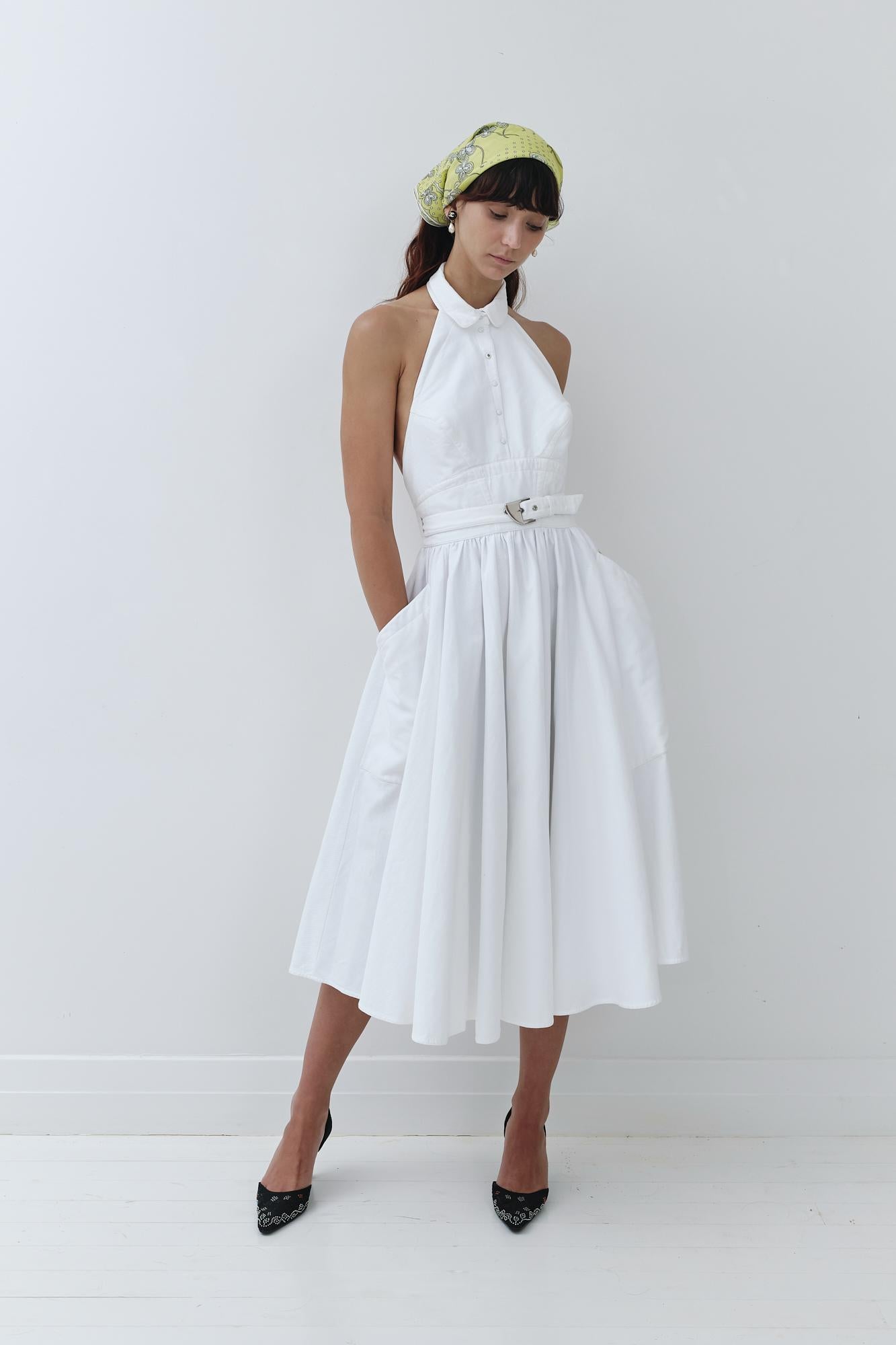Dating to the 80's, this stunning dress is an amazing example of Mugler's mastery of tailoring. Made from stiff cotton pique, it features a collared halter neck, nipped-in waist, full skirt with pockets and waist belt with a chunky silver buckle.