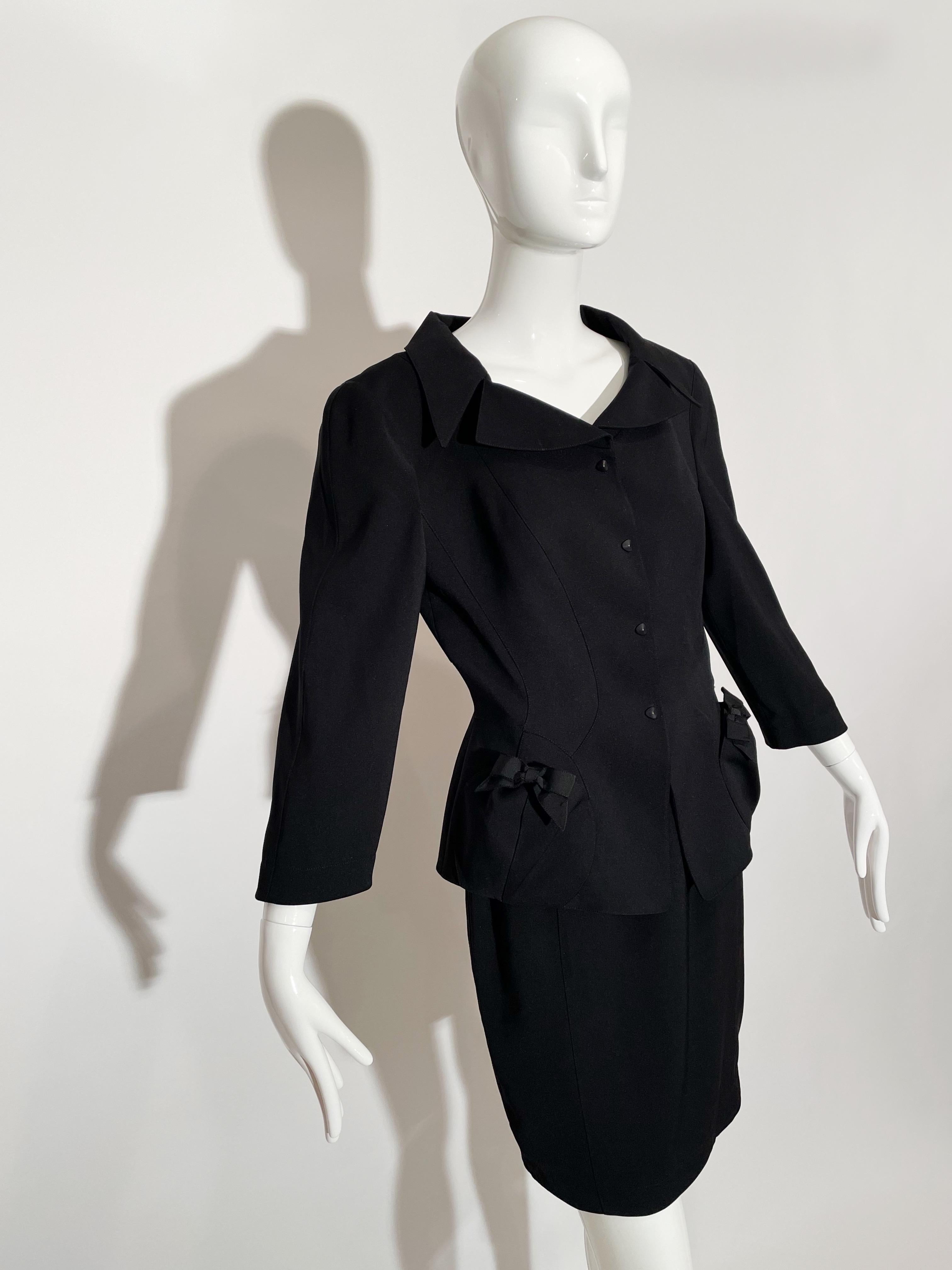 Black skirt suit. Bow detail on pockets. Front Pockets on waist of blazer. Button closures at front and wrist. Lapel collar. 3/4 length sleeves. Rear zipper closure on skirt. Rear pleat detail on skirt. Polyester. Lined. Made in France.

*Condition: