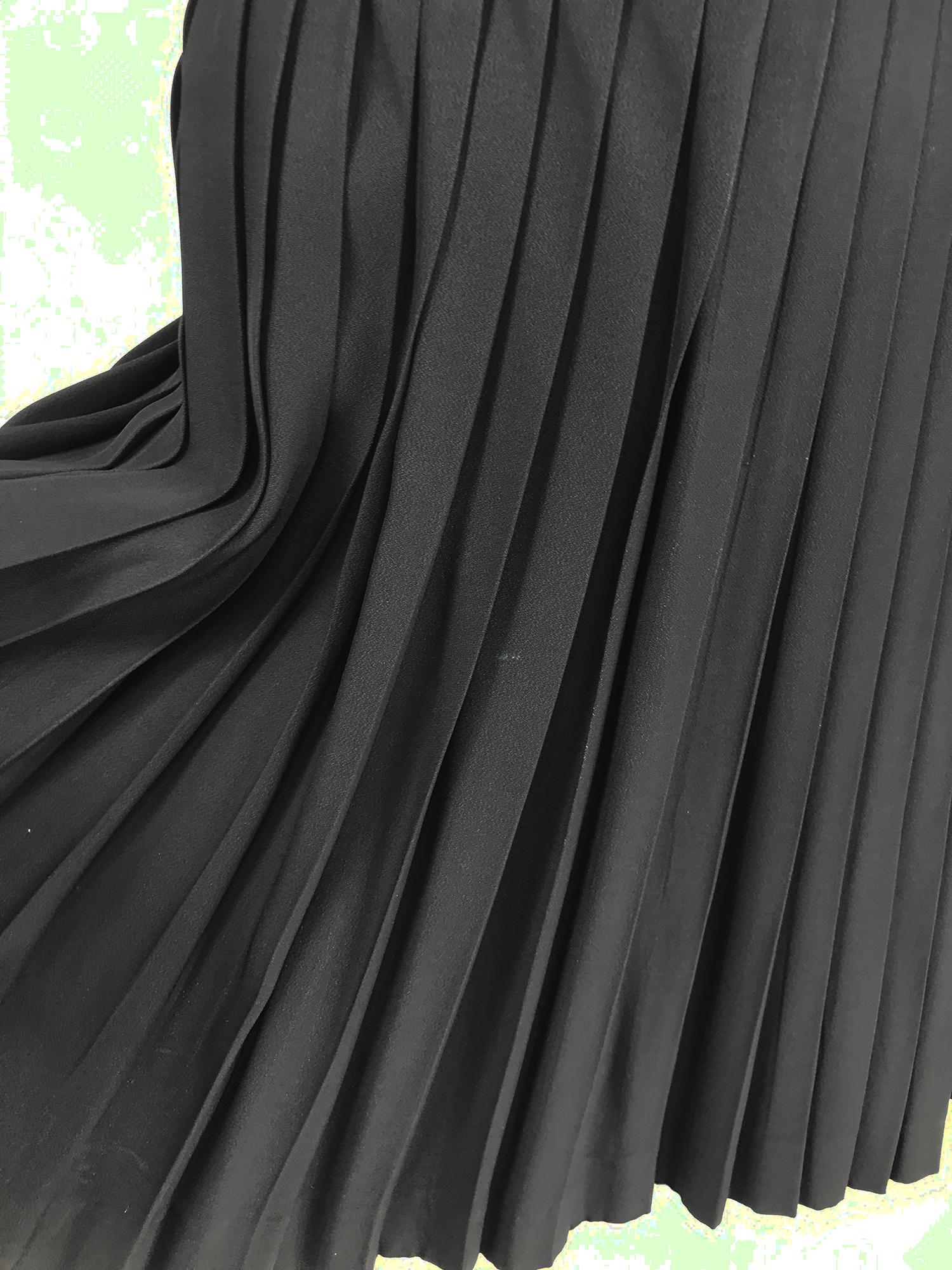 Schwarzer Satin-Minirock aus den 1980er Jahren mit seitlicher Druckknopfleiste und Plissee. Taillenband, offene Falten, Rock schließt an der Seite mit schwarzen, strukturierten Druckknöpfen, von der Taille bis zum Saum. Unbeschriftet. Markierte