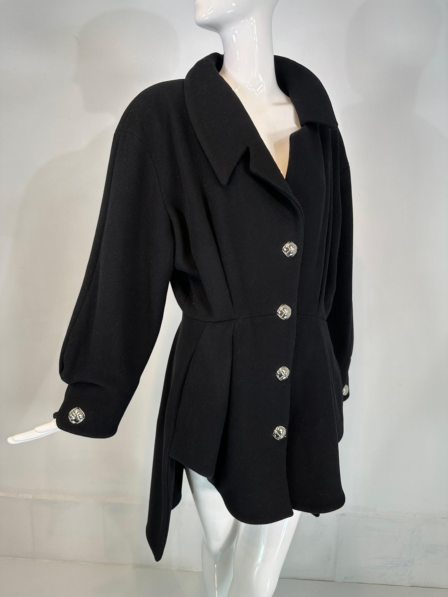 Manteau asymétrique en laine noire de Thierry Mugler avec boutons pression argentés au dos, années 1990, marqué taille EU44 (Italie).
Un manteau unique avec tous les détails que seul Thierry Mugler peut offrir. Ce manteau à simple boutonnage se