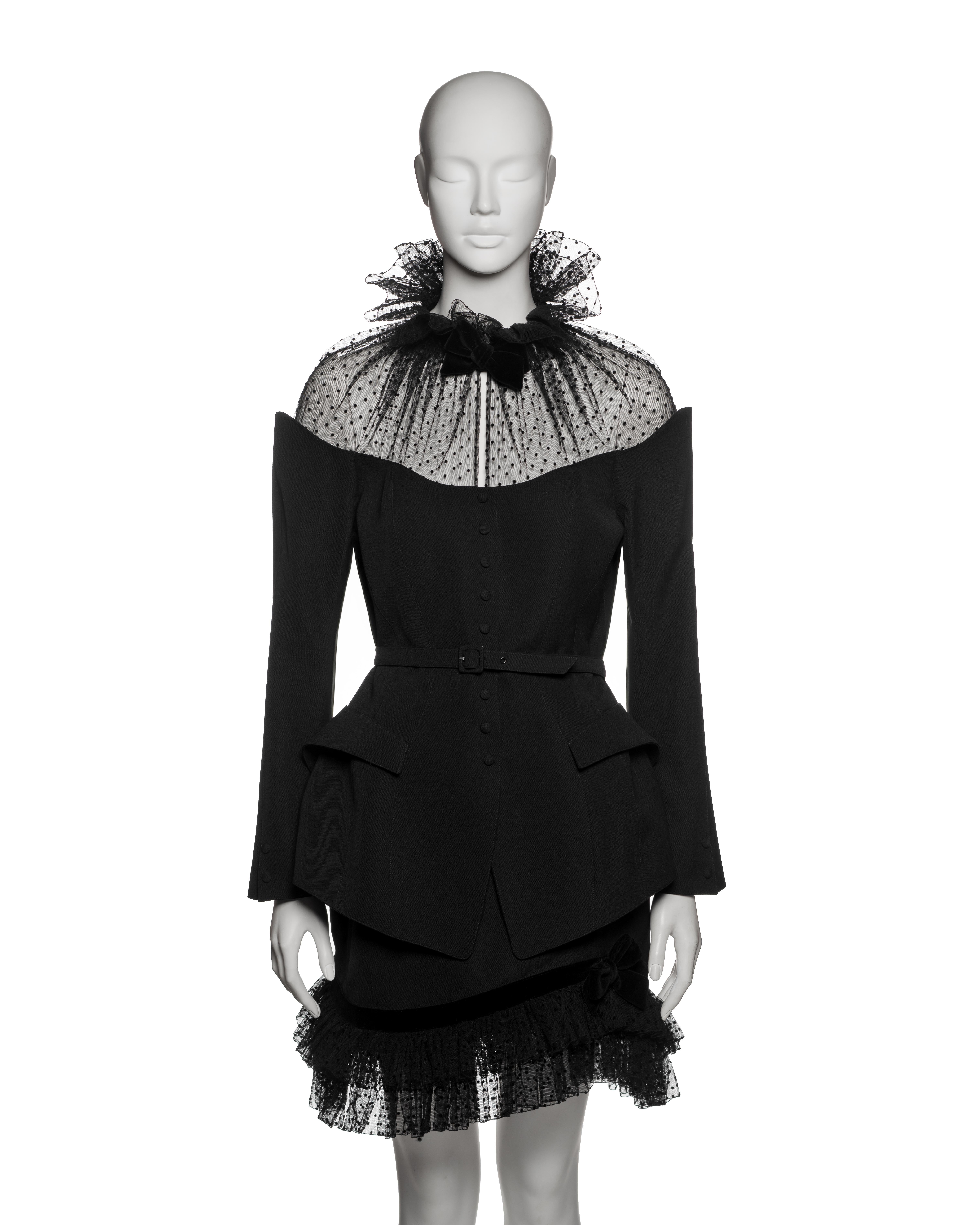 Tailored black wool suit by Thierry Mugler from the Fall-Winter 1995 collection, comprising a sharply sculpted belted jacket and matching mini skirt. The fitted jacket is constructed with Mugler’s signature hourglass silhouette, featuring a curved