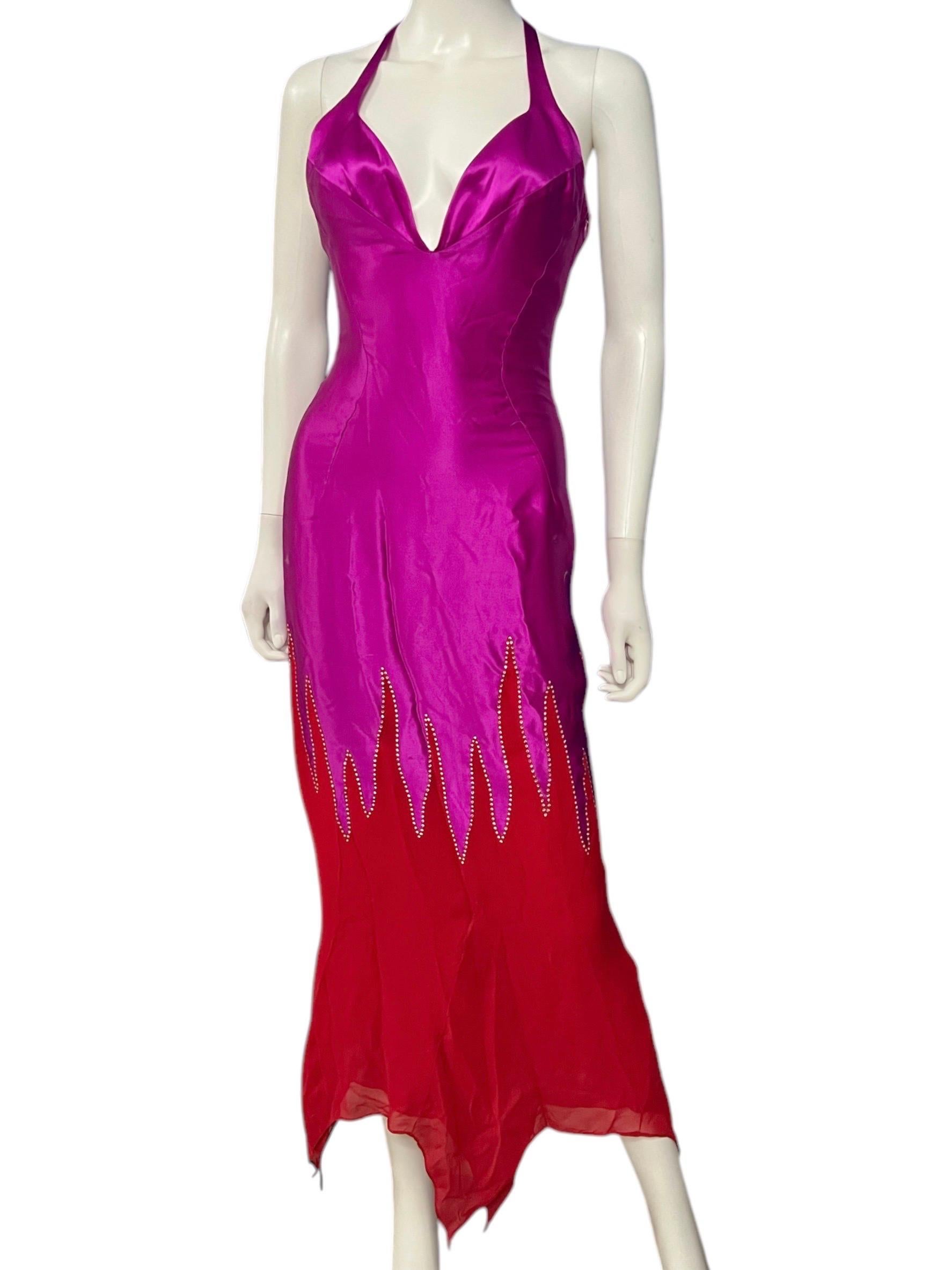 This early 2000’s vintage Thierry Mugler gown features a halter neckline with a plunging V-front. The dress transitions from vibrant fuchsia to deep red, with flame-like cutouts adorned with sparkling embellishments. An asymmetrical hemline adds a