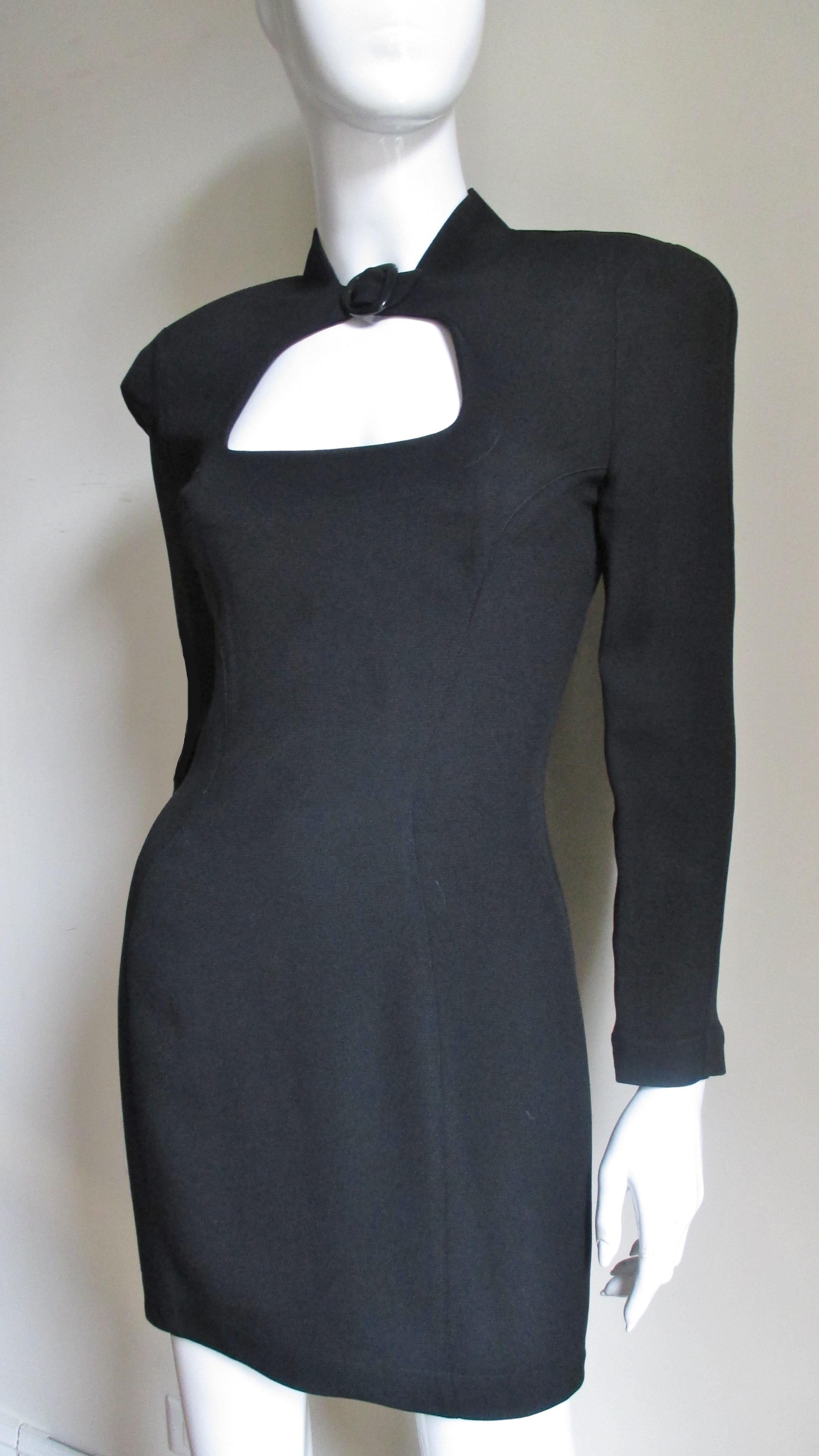 A fabulous black light weight wool dress from Thierry Mugler. It is semi fitted with long sleeves, a small black buckle at the front neck and a cut out below it.  The hemline is asymmetric.  It is fully lined, has lightly padded shoulders and a back