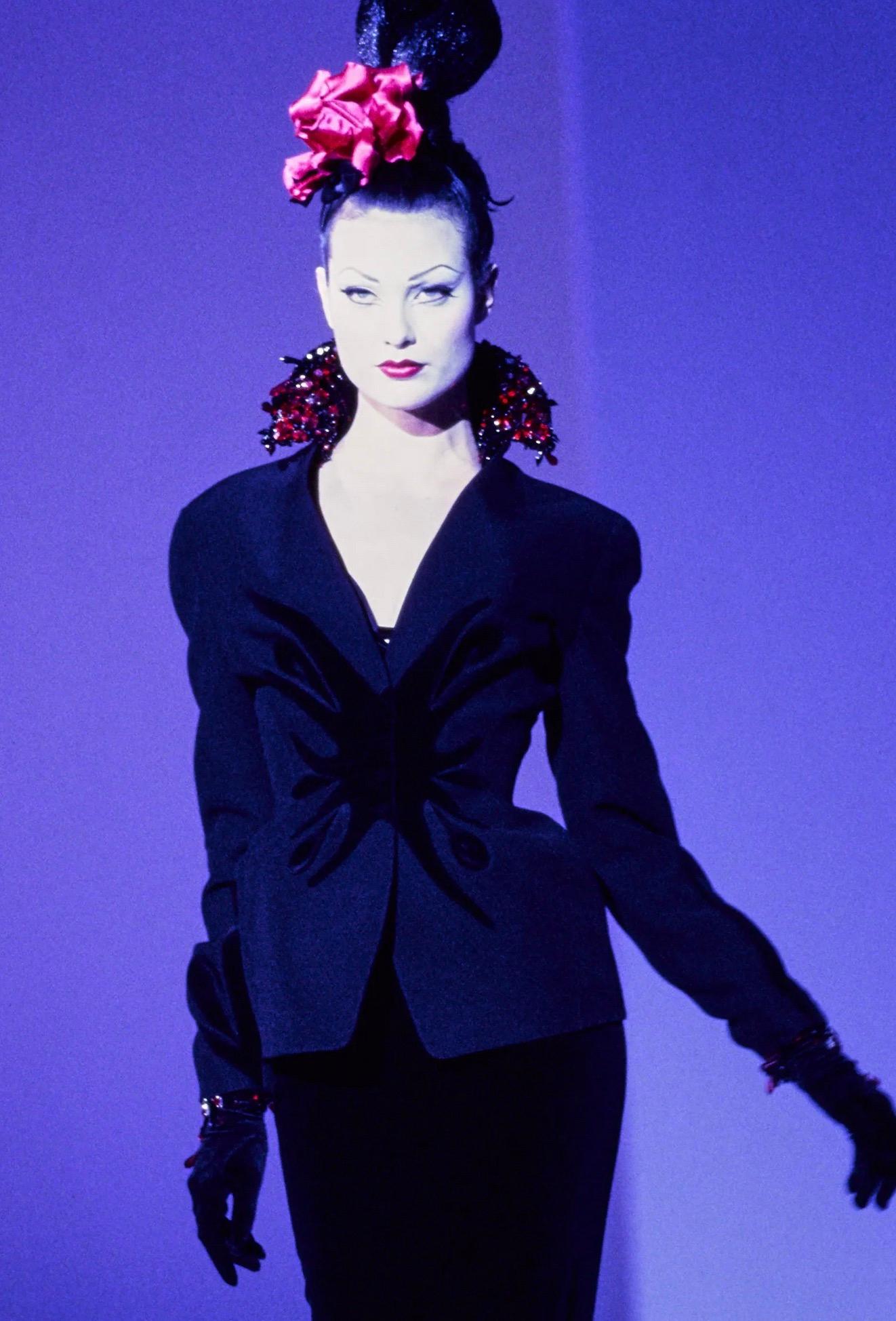 Nel cosmo teatrale della Collection'S di Thierry Mugler per l'Autunno Inverno 1995, dove la seduzione era scolpita nell'architettura e il glamour irradiava un'intensità quasi mitica, questo ensemble è emerso come una bellissima dichiarazione
