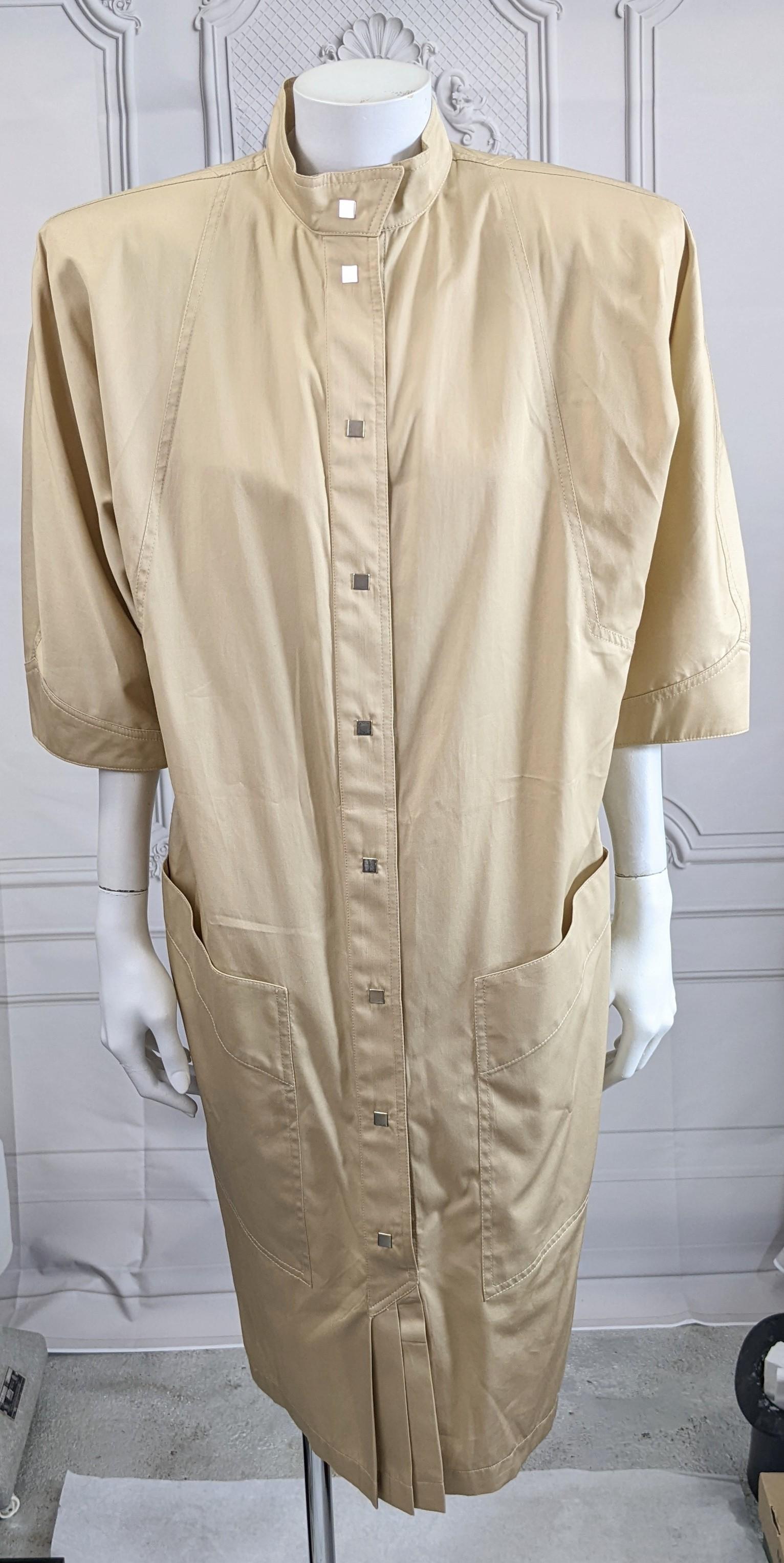 Statement Thierry Mugler Khaki Cotton Poplin Safari Dress with massive shoulder pads which tapers down to the hem. Front placket is closed with snaps to the knee where a series of pleats opens. Large important shoulders with cropped sleeves, and