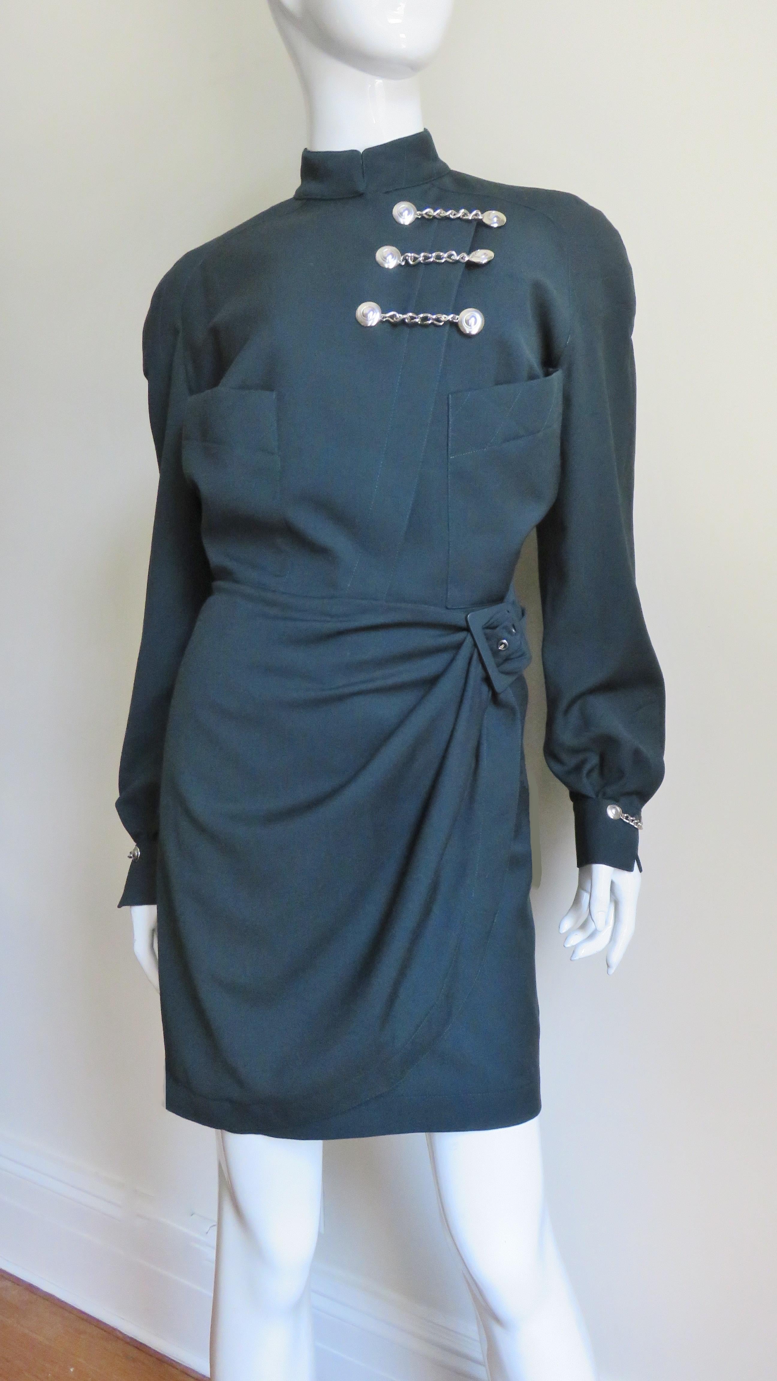 A fabulous forest green wool military influence dress by Thierry Mugler.  It has a small stand up collar, long sleeves with cuffs and 2 bodice patch pockets. The dress skirt wraps across the front closing at the side with a matching green buckle. 