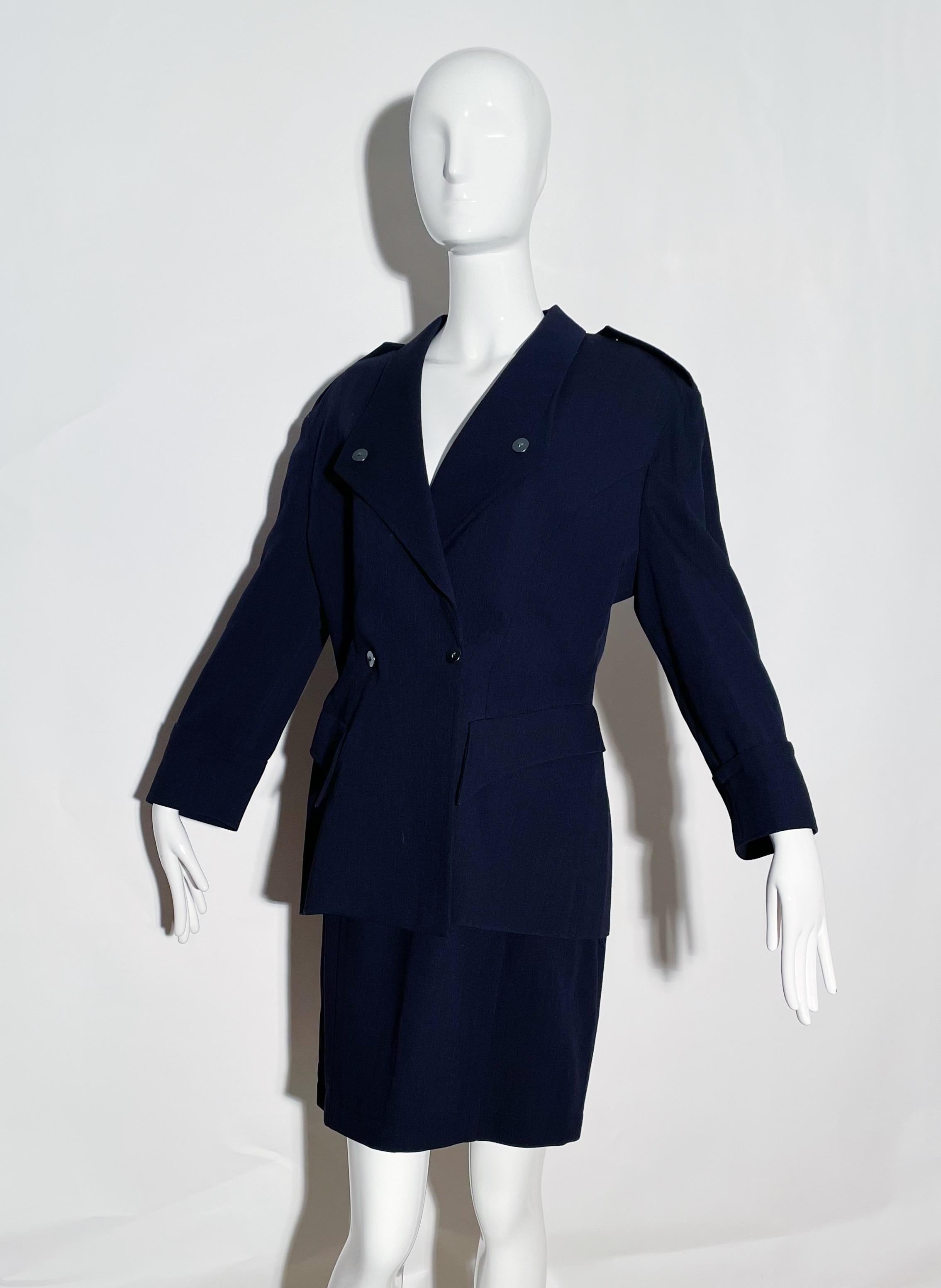 Navy skirt suit. Front snap closures. Lapel. Front pockets. Lined. Shoulder pads Rear zipper closure on skirt. Wool. Made in France. 
*Condition: Excellent vintage condition. No visible Flaws.

Measurements Taken Laying Flat (inches)—
Shoulder to