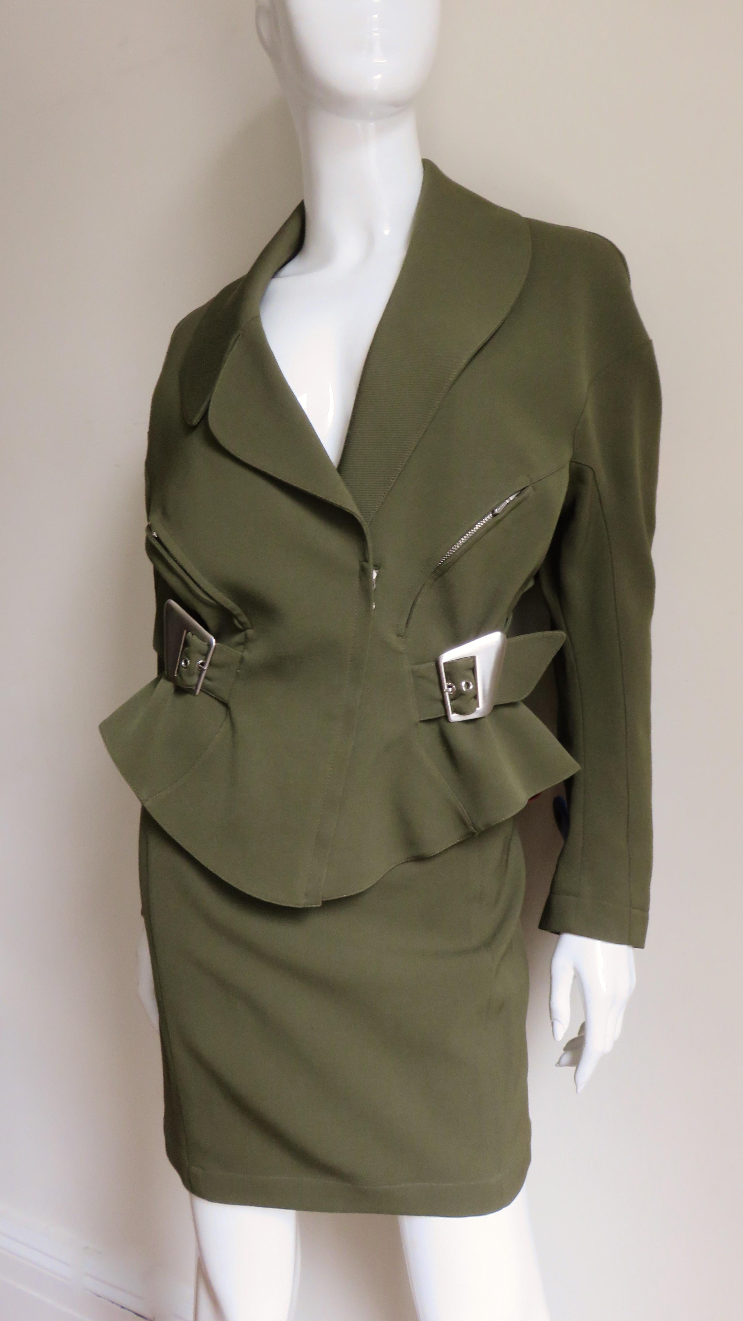 A fabulous olive green wool skirt suit from Thierry Mugler.  The jacket is rich in detail- curved seams with zipper pockets, an lapel collar and long seamed sleeves.  It has a back half belt closing with silver buckles on each side waist and a front