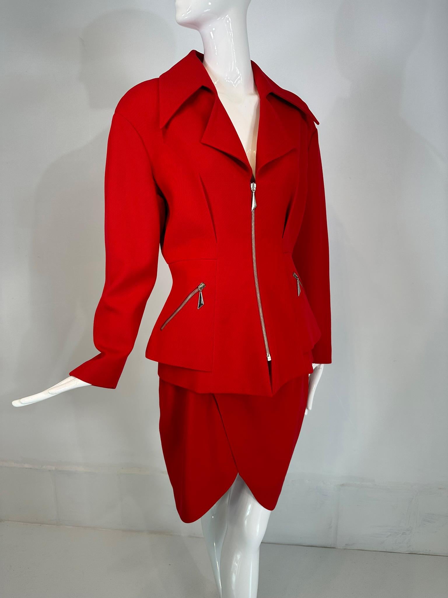 Set giacca e gonna di Thierry Mugler in lana rossa, con ampio bavero e vita a nip, con finiture in argento. 
La giacca in twill di lana rosso rossetto ha revers larghi e profondi e una scollatura a V. Darte in vita e peplum sui fianchi. Ci sono