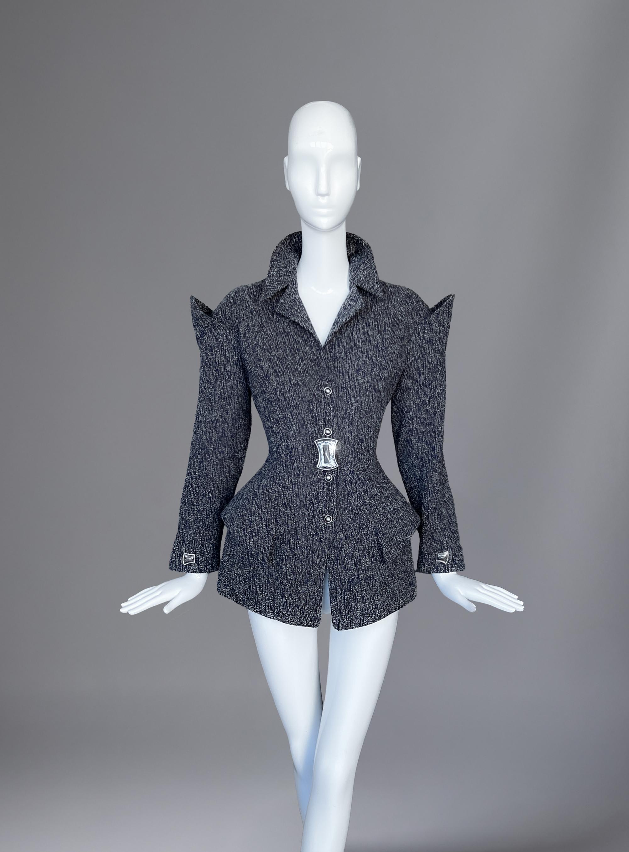 In this extraordinary creation from Thierry Mugler’s Fall 1995 collection, tailoring becomes seduction. The structured tweed jacket, at once architectural and sensual, sculpts the female form into a living sculpture. Stunning, angular shoulders jut