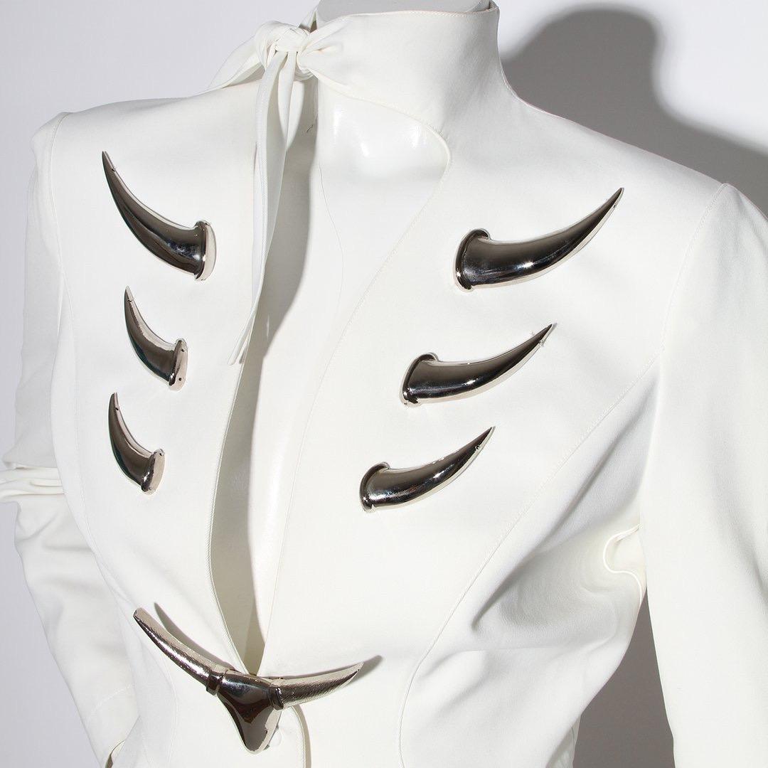 Thierry Mugler Skirt Suit 
Spring / Summer 1992 Ready-to-Wear Collection 
Made in France 
White 
Fitted jacket
Two snap closures in front of jacket 
Tie at neck 
Silver horn hardware details on front of jacket 
Two silver horn hardware details on
