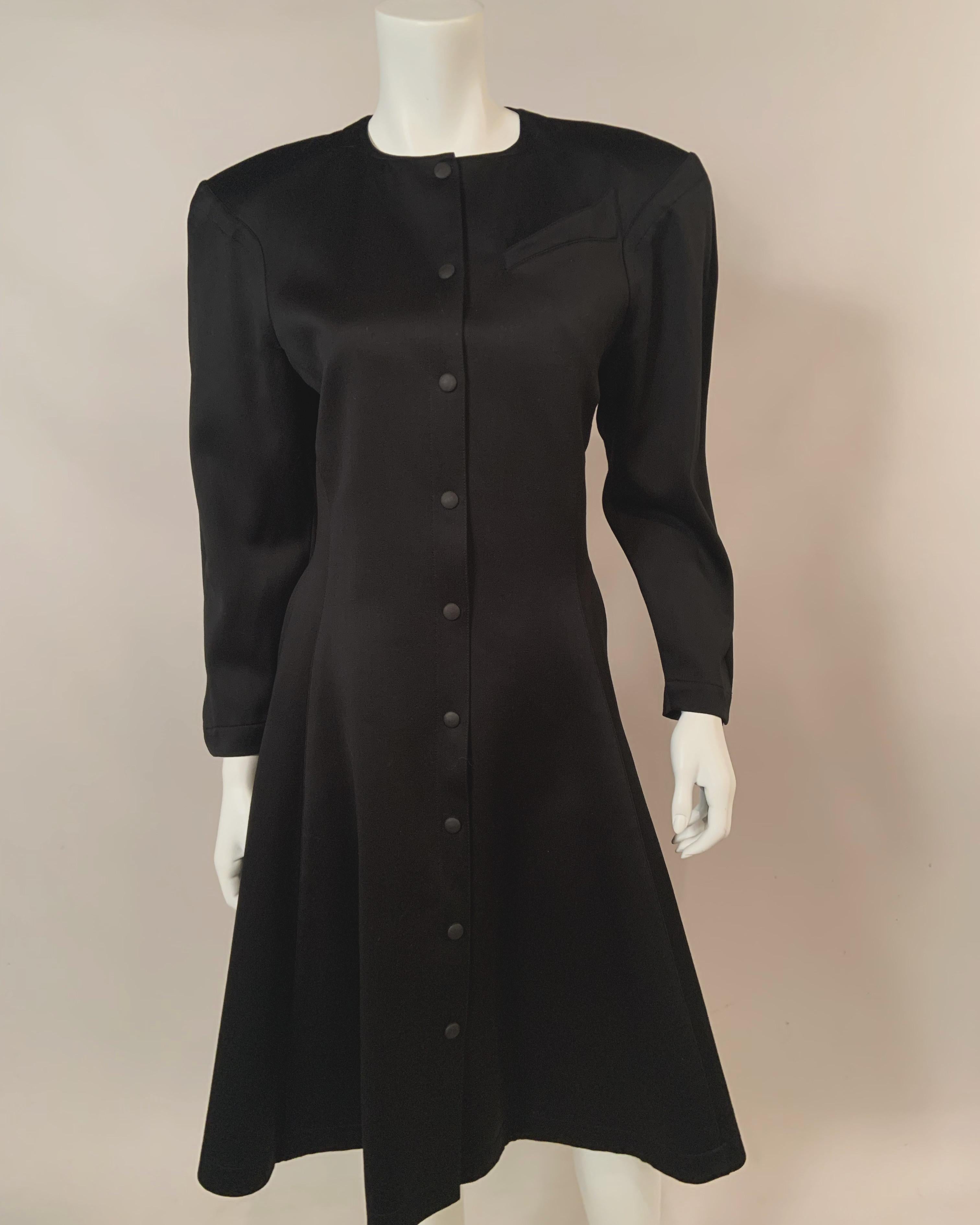 Thierry Mugler a conçu une robe de dîner ou de cocktail chic en laine noire avec une fermeture à boutons-pression de l'encolure à l'ourlet.
La robe a une ligne d'épaule forte avec des tampons d'épaule optionnels et une bande d'un pouce de large à la