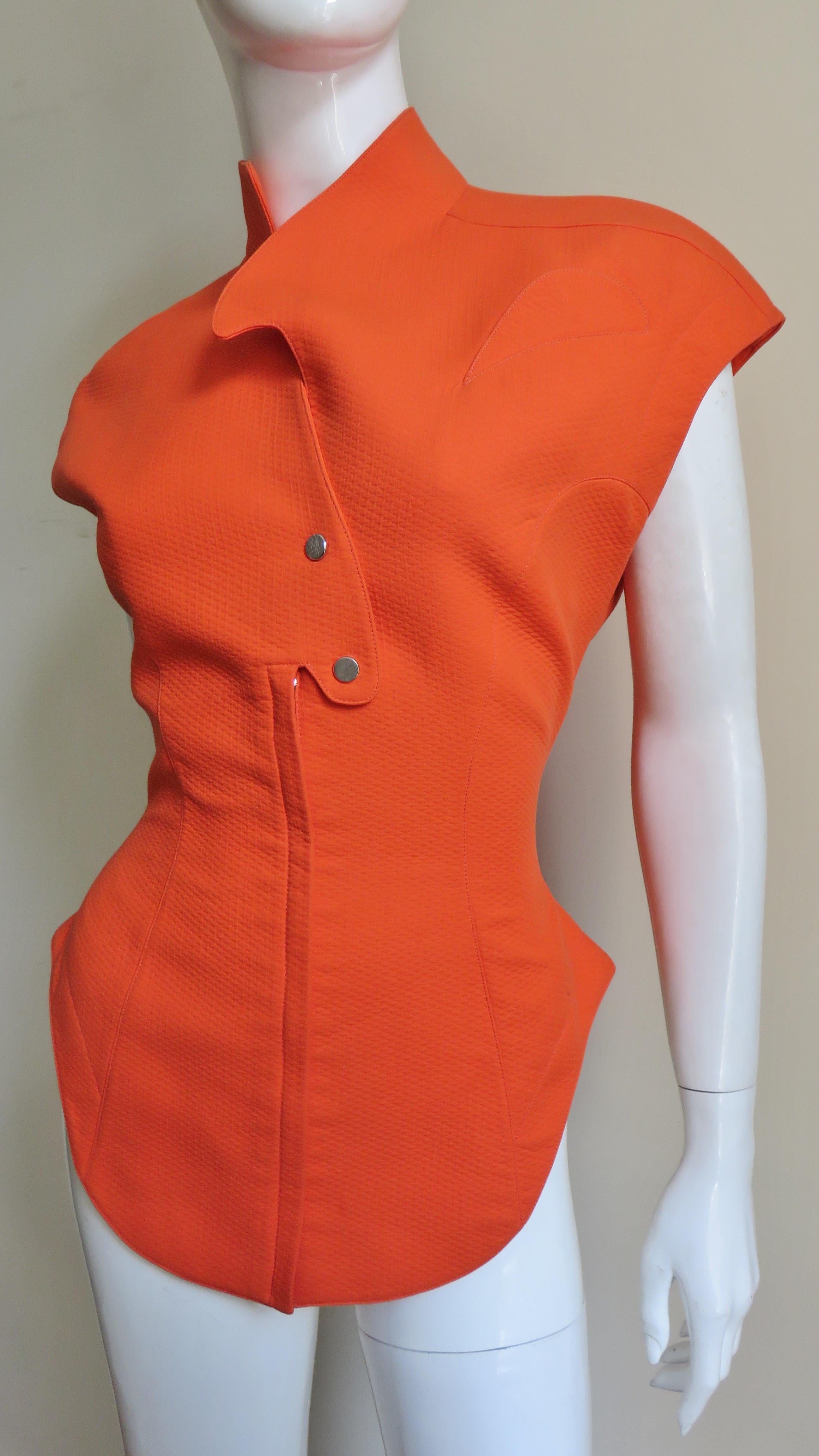 A fabulous jacket, top in orange cotton from Thierry Mugler.  It has extended shoulders forming cap sleeves, a curved stand up collar, shirt tail hem, a small curved chest pocket, and seaming cinching in the waist.  The top is fully lined and closes