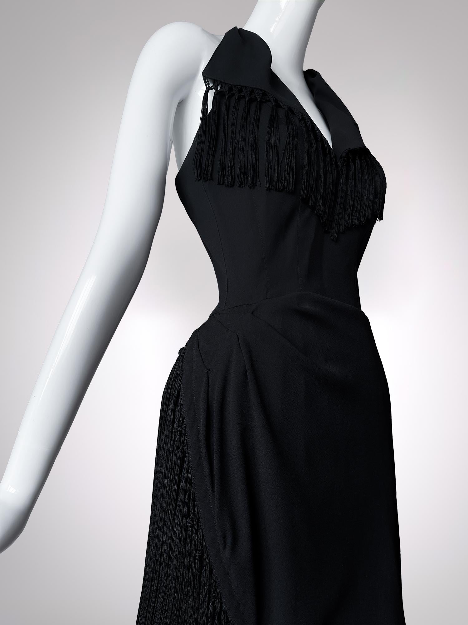 In diesem atemberaubenden schwarzen Kleid verbindet Thierry Mugler seine charakteristische skulpturale Präzision mit Bewegung. Die Silhouette ist rasiermesserscharf und schmiegt sich mit chirurgischer Präzision an den Körper, während strategische